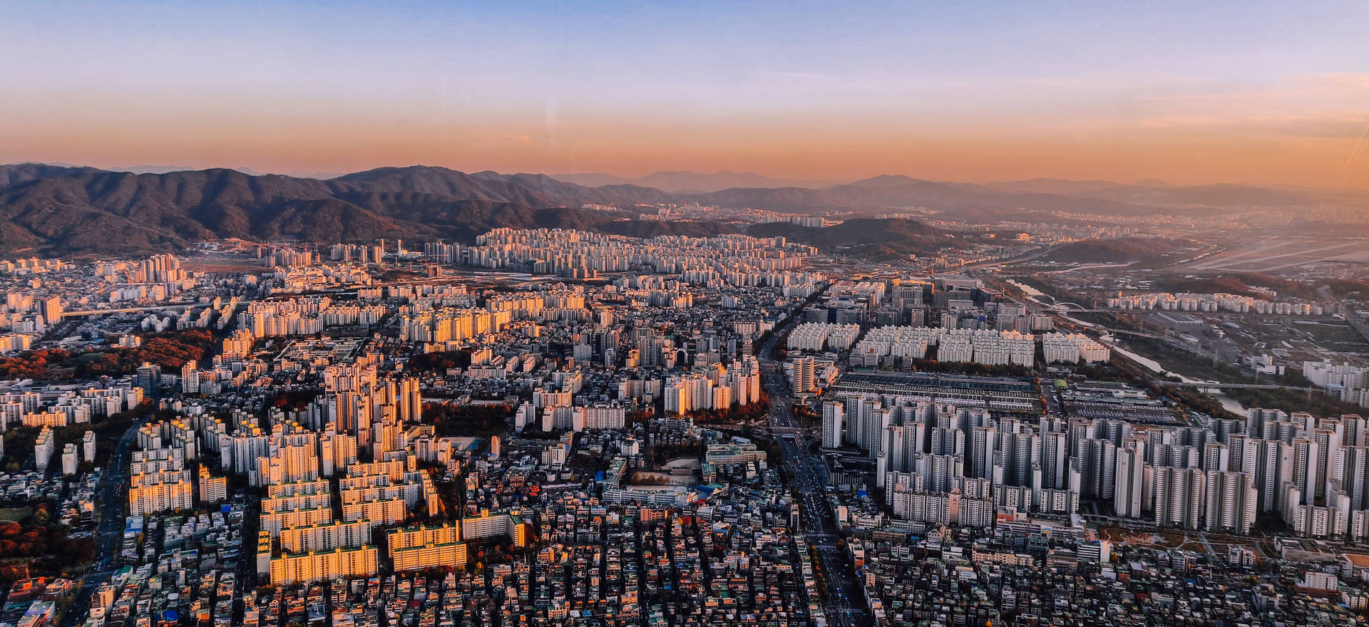 日落時的城市景觀，背景有山，建築物上灑滿金色陽光。
