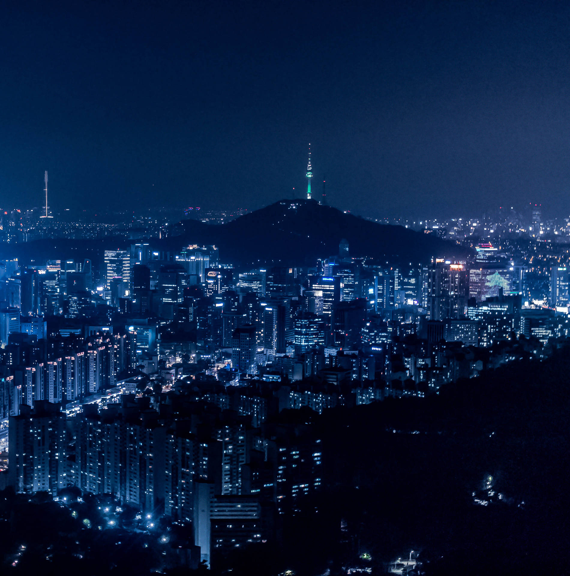密集城市的夜景，有燈光建築物和山丘上的塔樓。