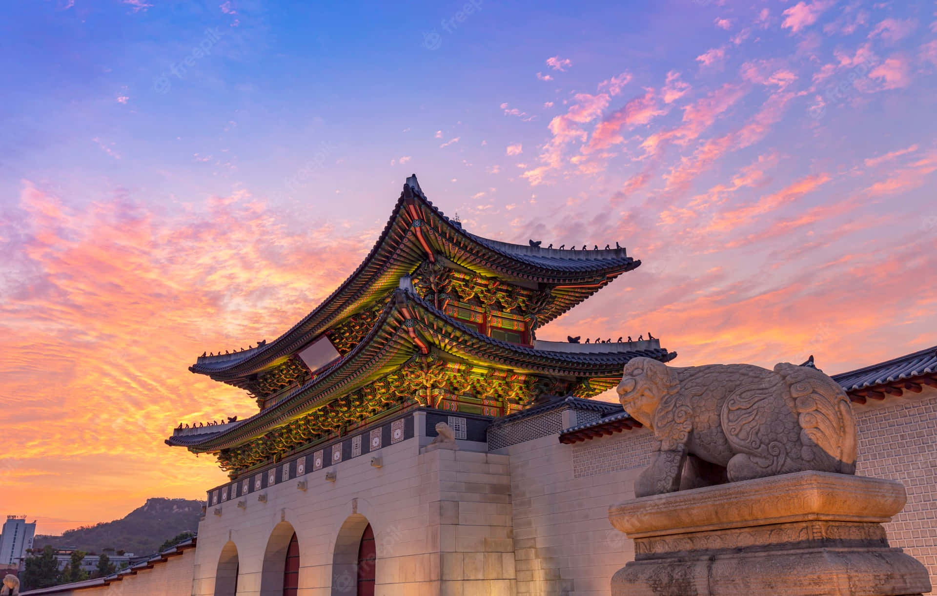 首爾景福宮夕照天空 壁紙 — 傳統韓國宮殿大門在充滿活力的日落天空下閃耀，天空有粉橙色雲彩，前景有石獅守護。