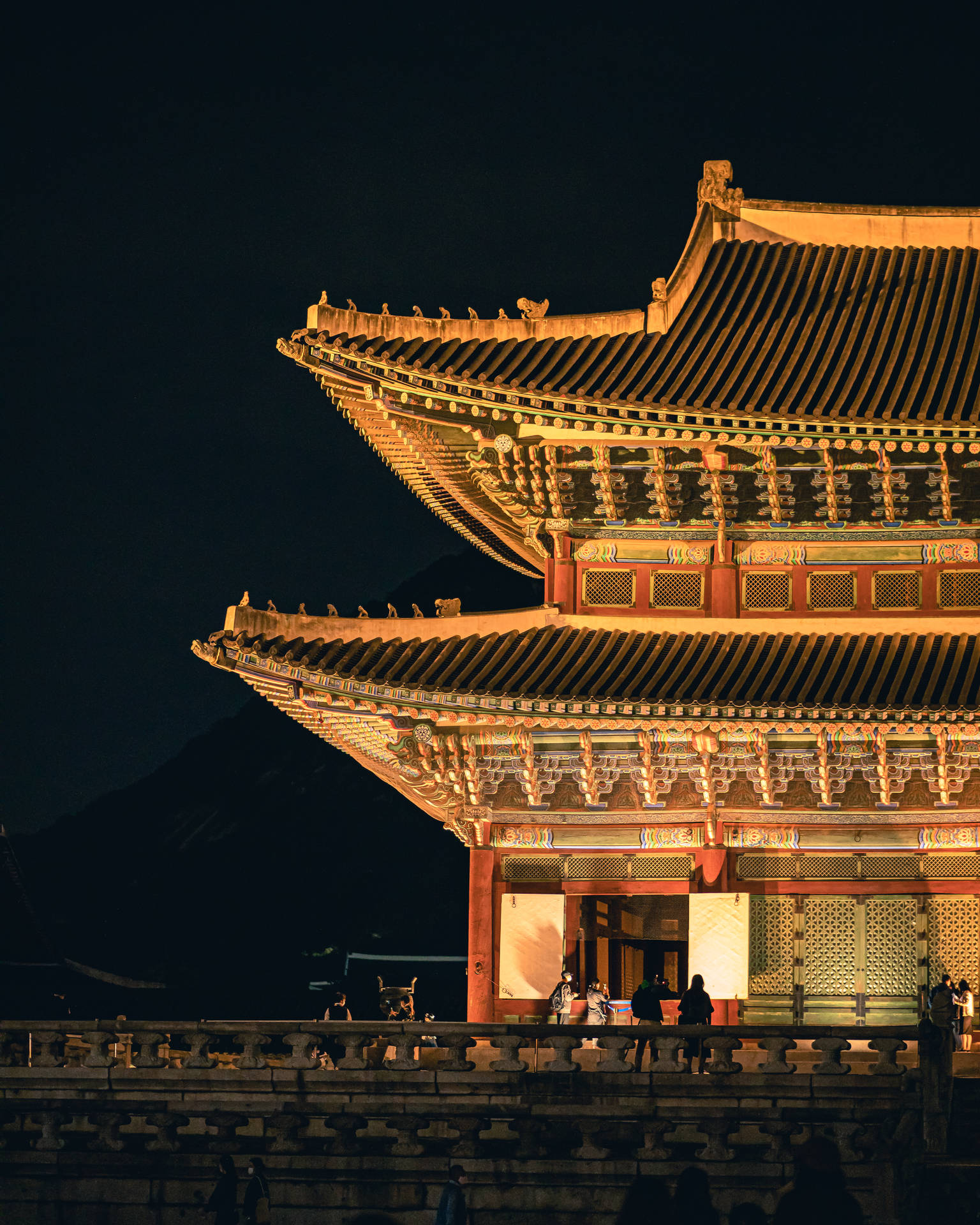 夜間點亮的傳統韓國宮殿，遊客在石牆上。
