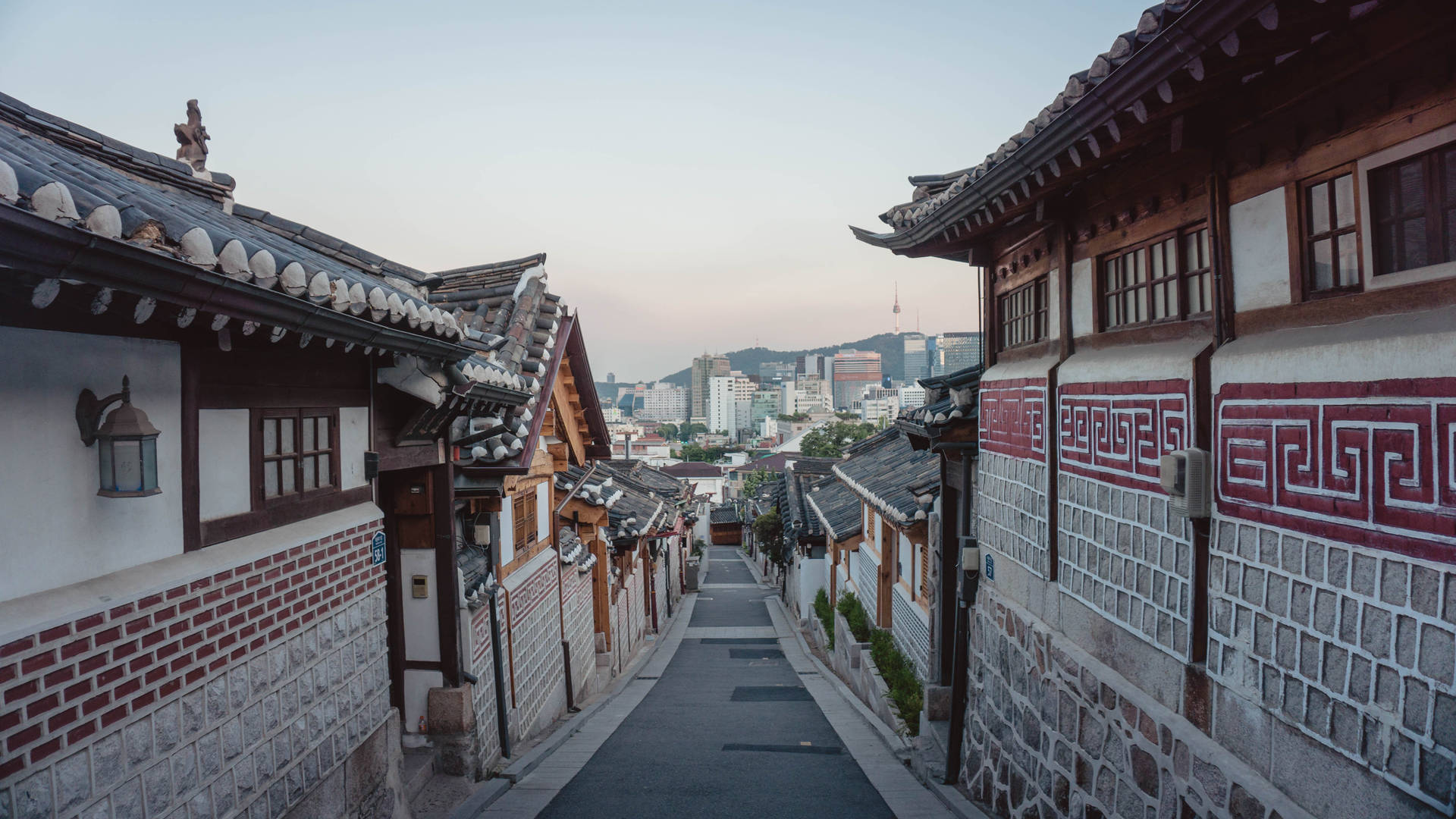 傳統韓國房屋排列在一條狹窄的小巷中，通往黃昏時分的現代城市天際線。