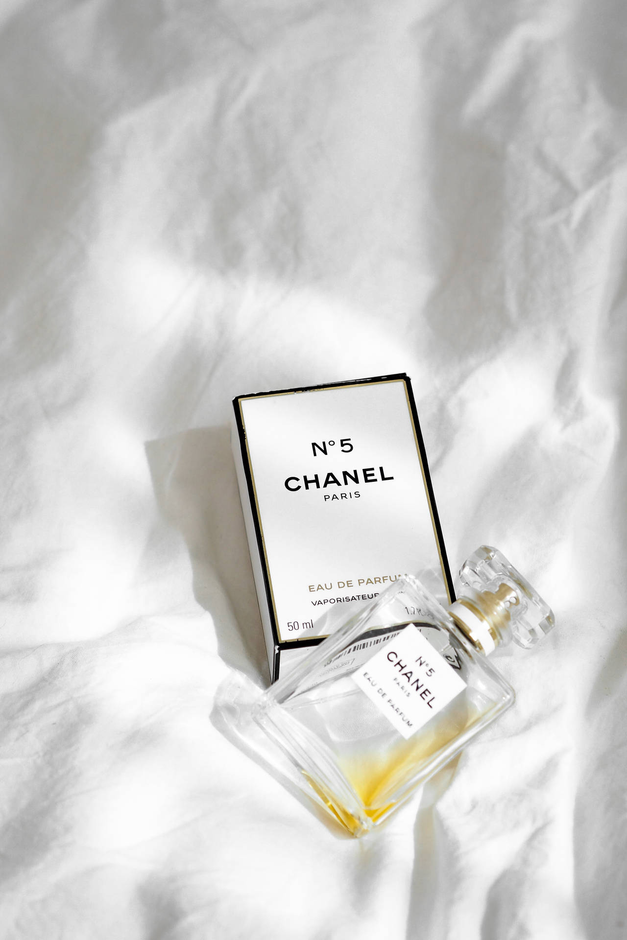 Chanel No 5 香水瓶和盒子放在白色布上，帶有柔和陰影。