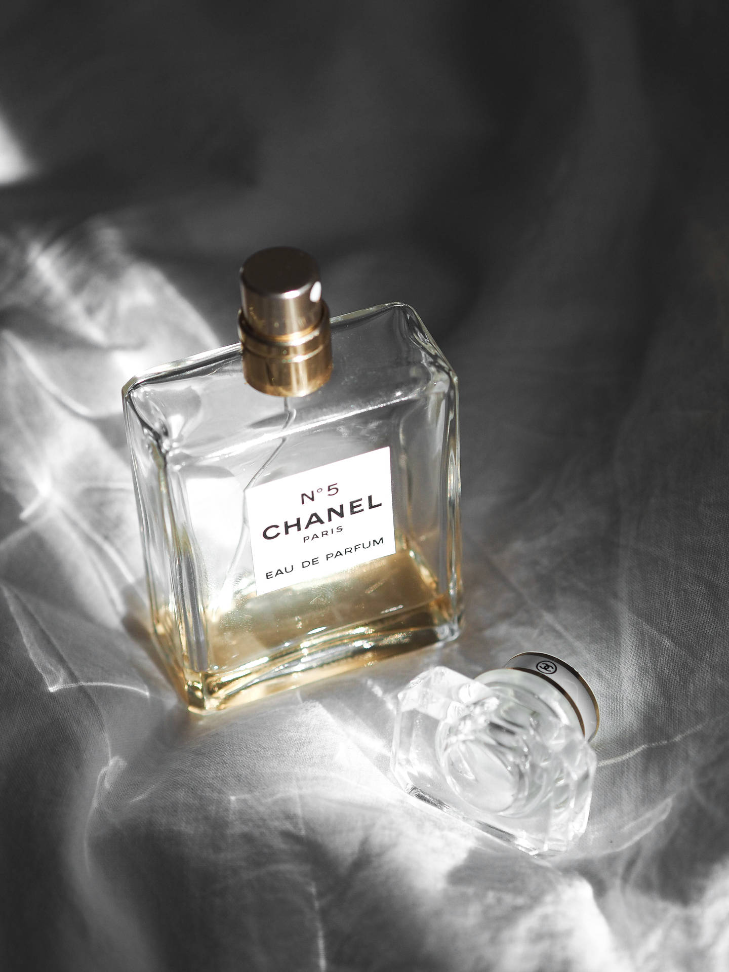 Chanel No 5 香水瓶放在有紋理的銀色布料上，柔和光線。