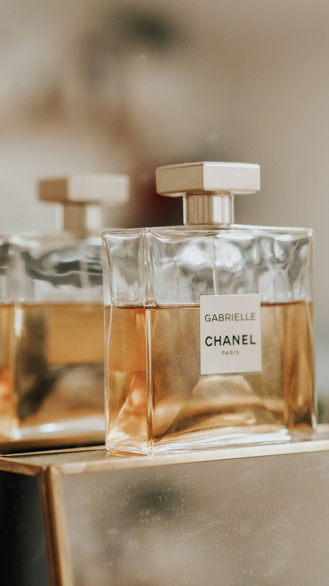 兩瓶 Chanel Gabrielle 香水放在金色表面上，光線柔和。