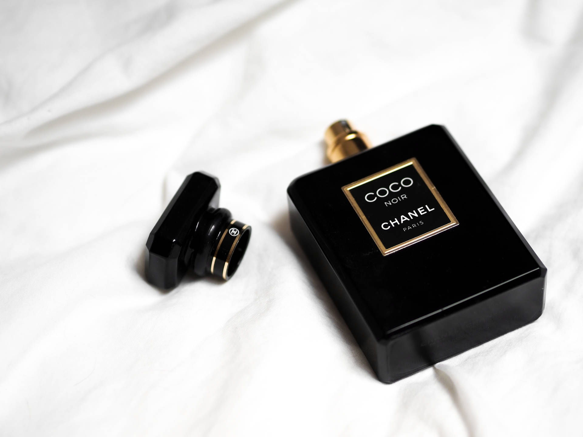 黑色 Chanel Coco Noir 香水瓶，金色瓶蓋，置於白色布料上。