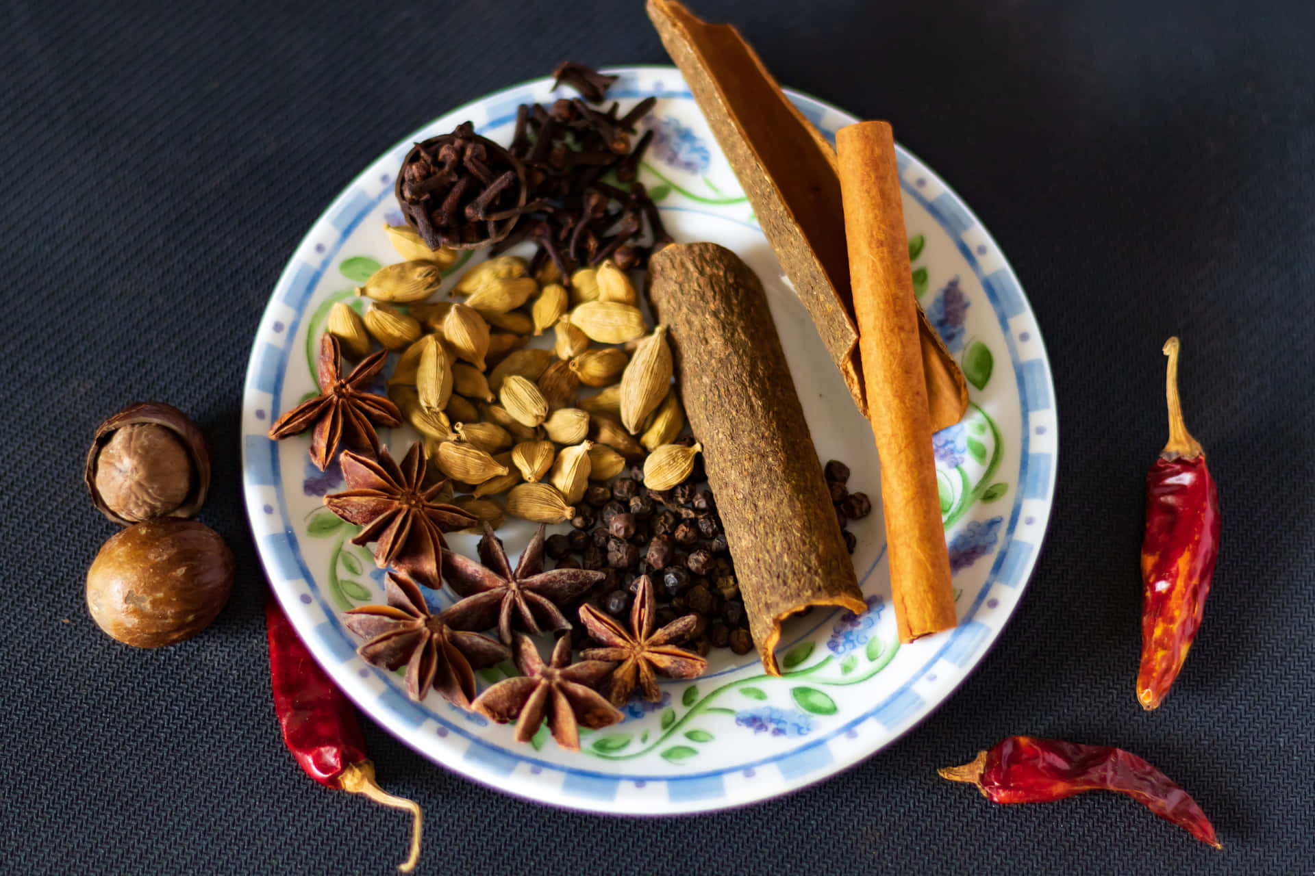 一個盛載原粒香料和乾紅辣椒的盤子，放在深色紋理表面上。