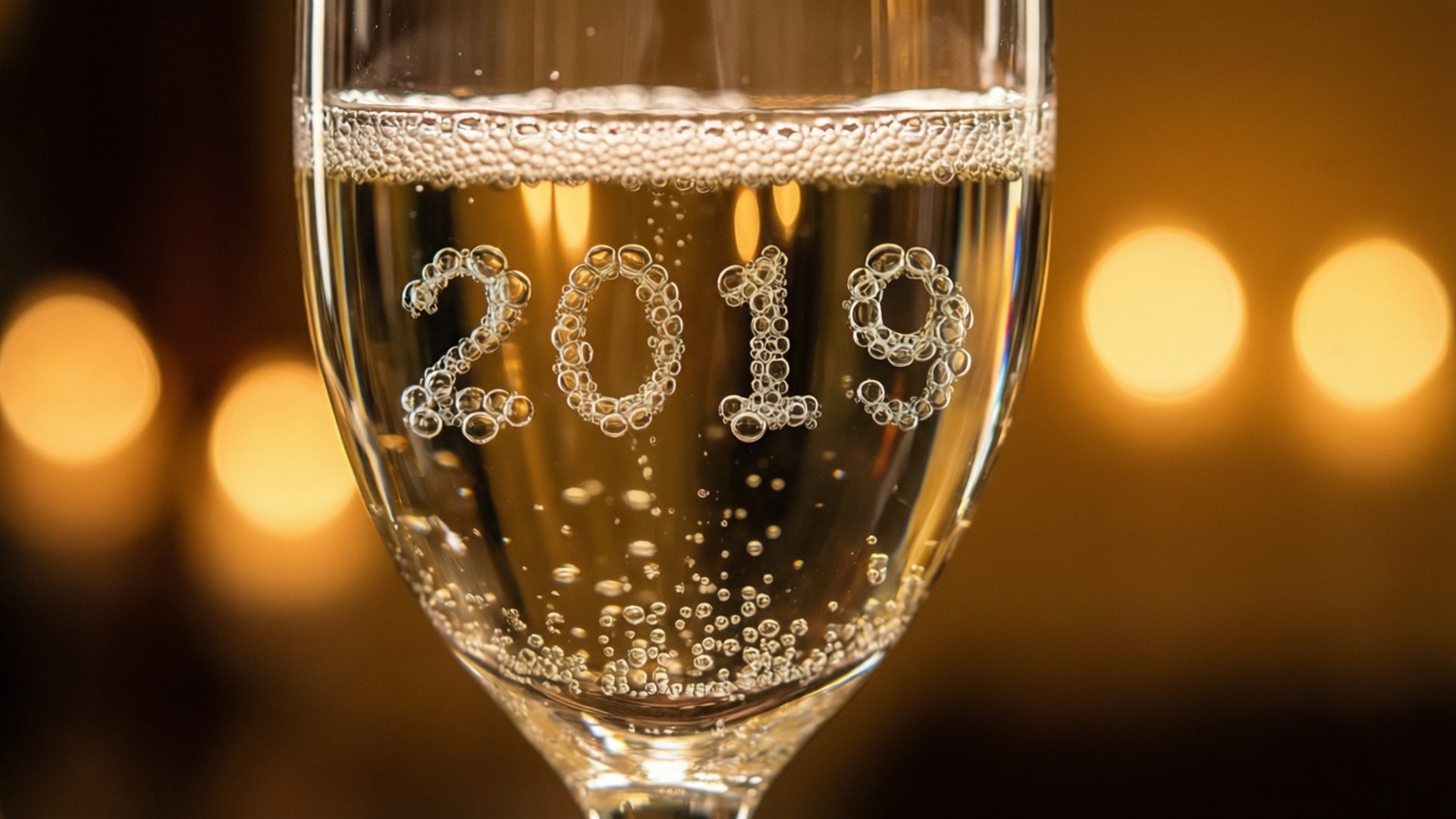 香檳杯中的氣泡拼出2019，金色燈光下。