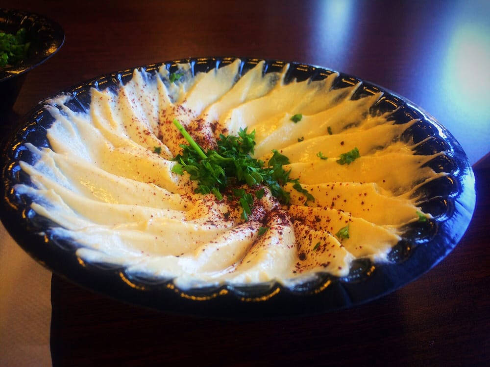 香氣四溢的鵝肝醬，頂上撒有豐富香料與新鮮香草 壁紙 — 一個奶油鷹嘴豆泥在深色波浪碗中巧妙地扇形展開，上面撒有紅椒粉和新鮮歐芹。