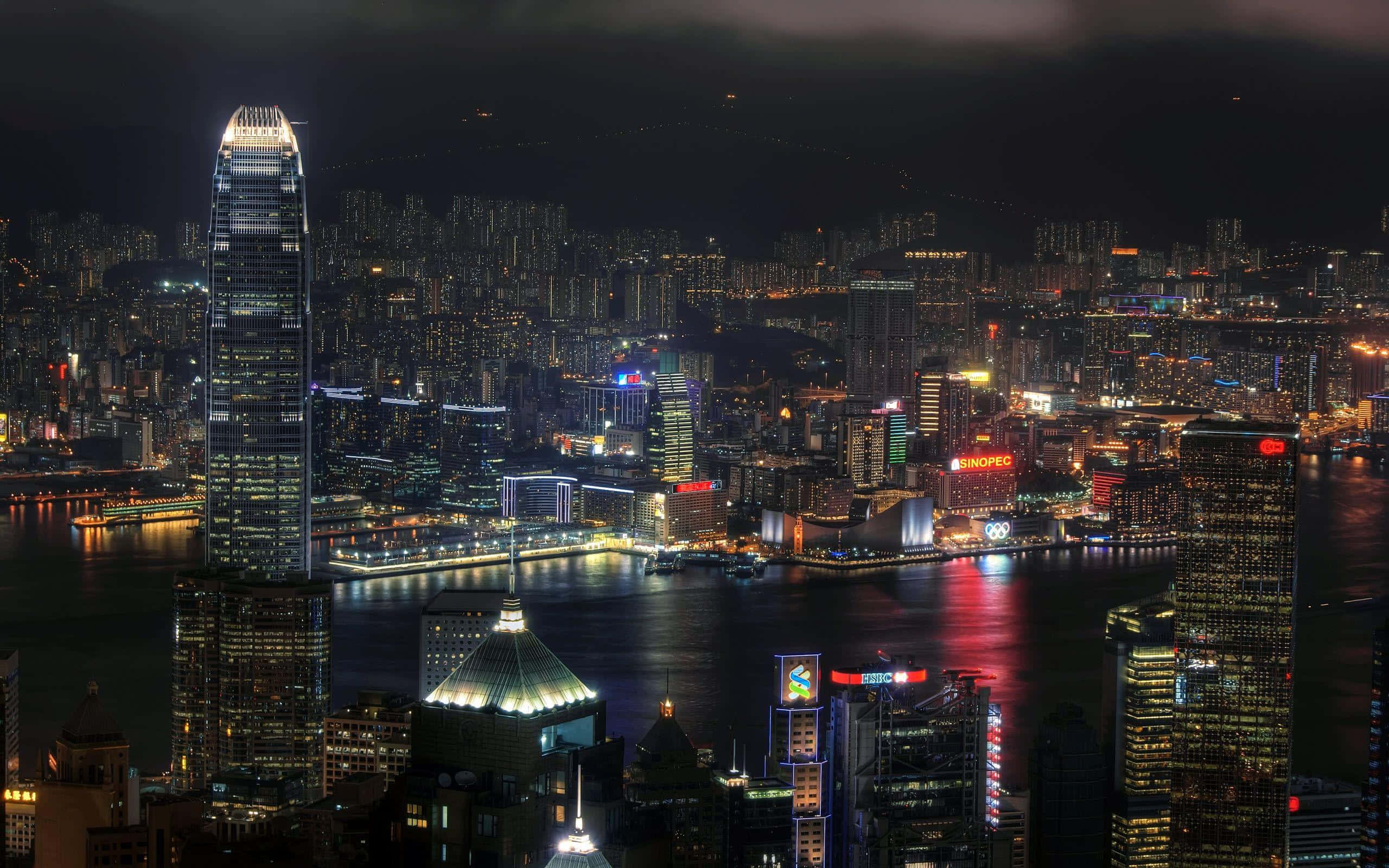 暗夜城市 桌布 壁紙 — 香港令人目眩的夜景，高聳的摩天大樓和閃爍的霓虹燈光倒映在港灣水面上。