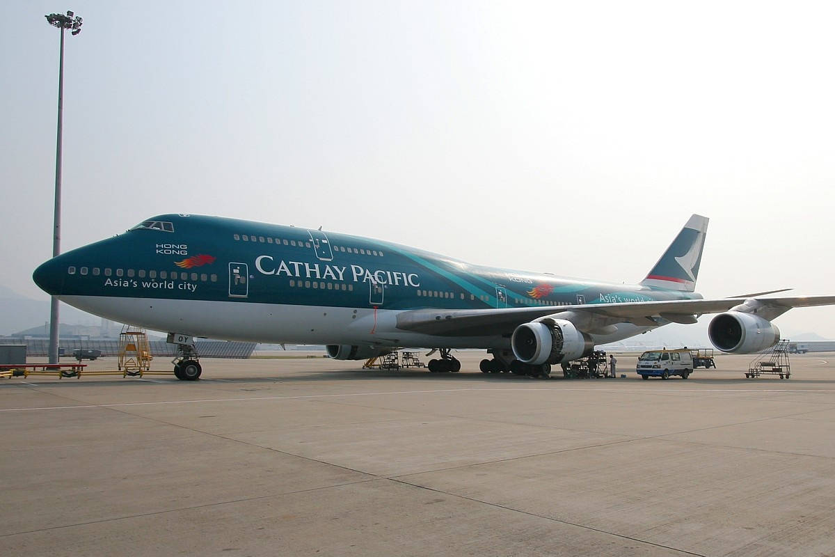 國泰航空波音747在機場停機坪上，有地勤人員和設備。