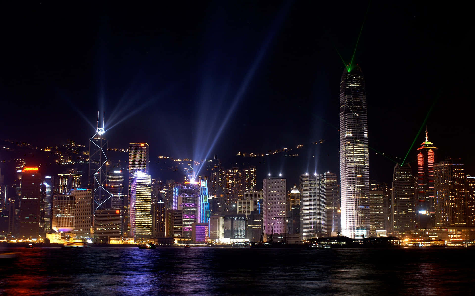 Buildings 桌布 壁紙 — 香港夜景，天際線上有耀眼的激光束和色彩繽紛的摩天大樓燈光，倒映在水面上。