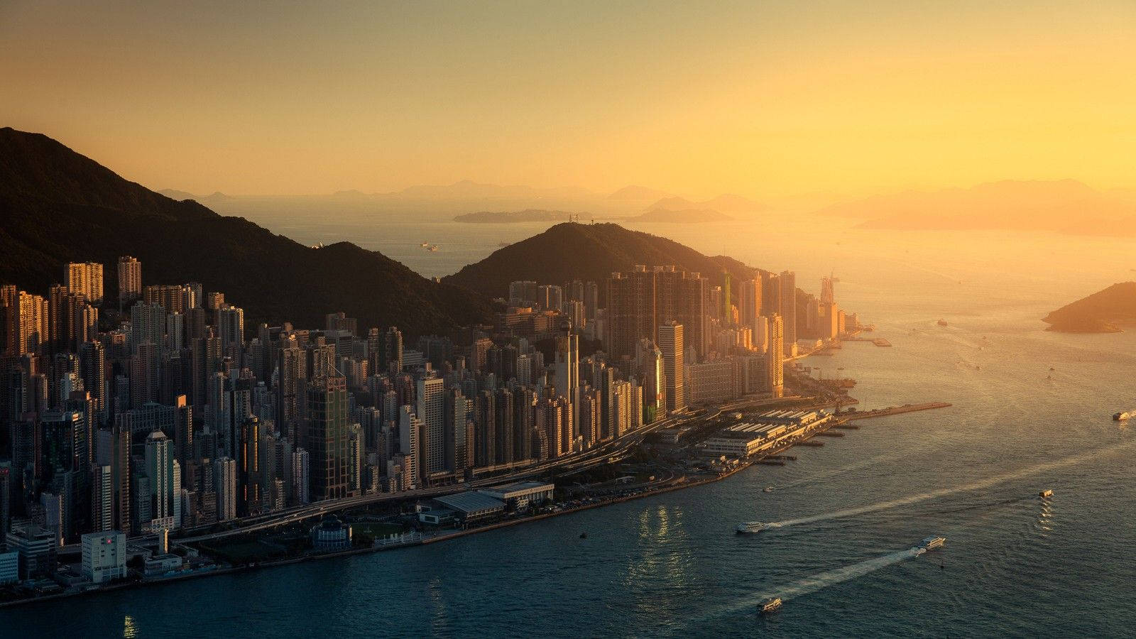金色夕陽下的香港天際線，港口上有船隻。