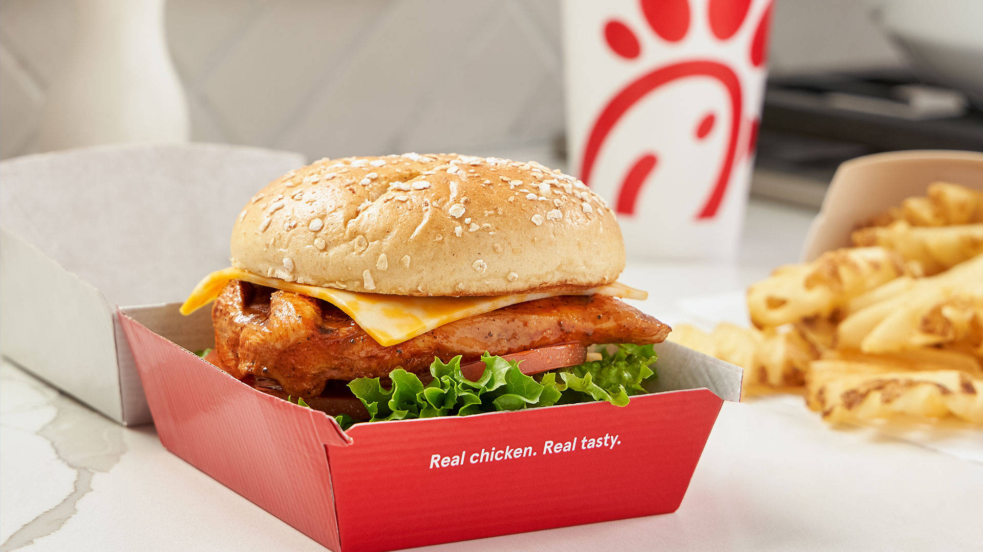 香濃 Chick-fil-A 雞肉三明治 壁紙 — 一個酥脆的雞肉三明治，配上融化的芝士和新鮮生菜，放在紅色Chick-fil-A盒子裡，旁邊有窩夫薯條和品牌飲料杯。