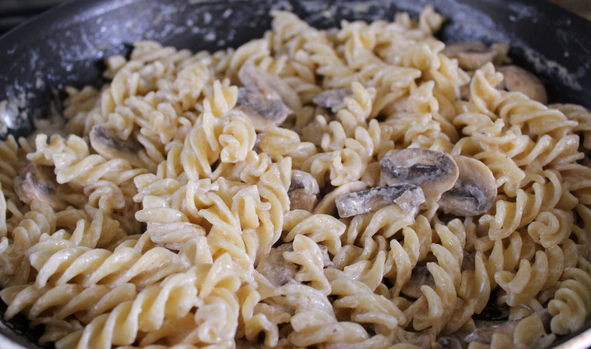 香濃 linguine 麵配洋蔥與鯖魚 壁紙 — 忌廉蘑菇意粉特寫，置於深色煎鍋中，閃亮醬汁包裹螺旋麵條。