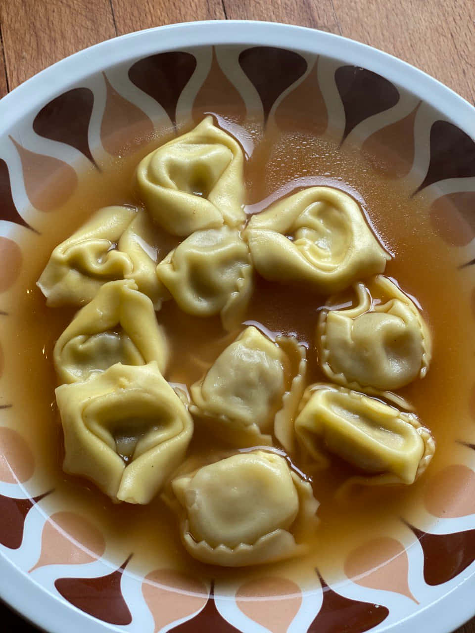 香濃家常布羅多湯通心粉 壁紙 — 一碗金黃色餃子浮在濃湯中，放在木桌上的圖案碟子上。