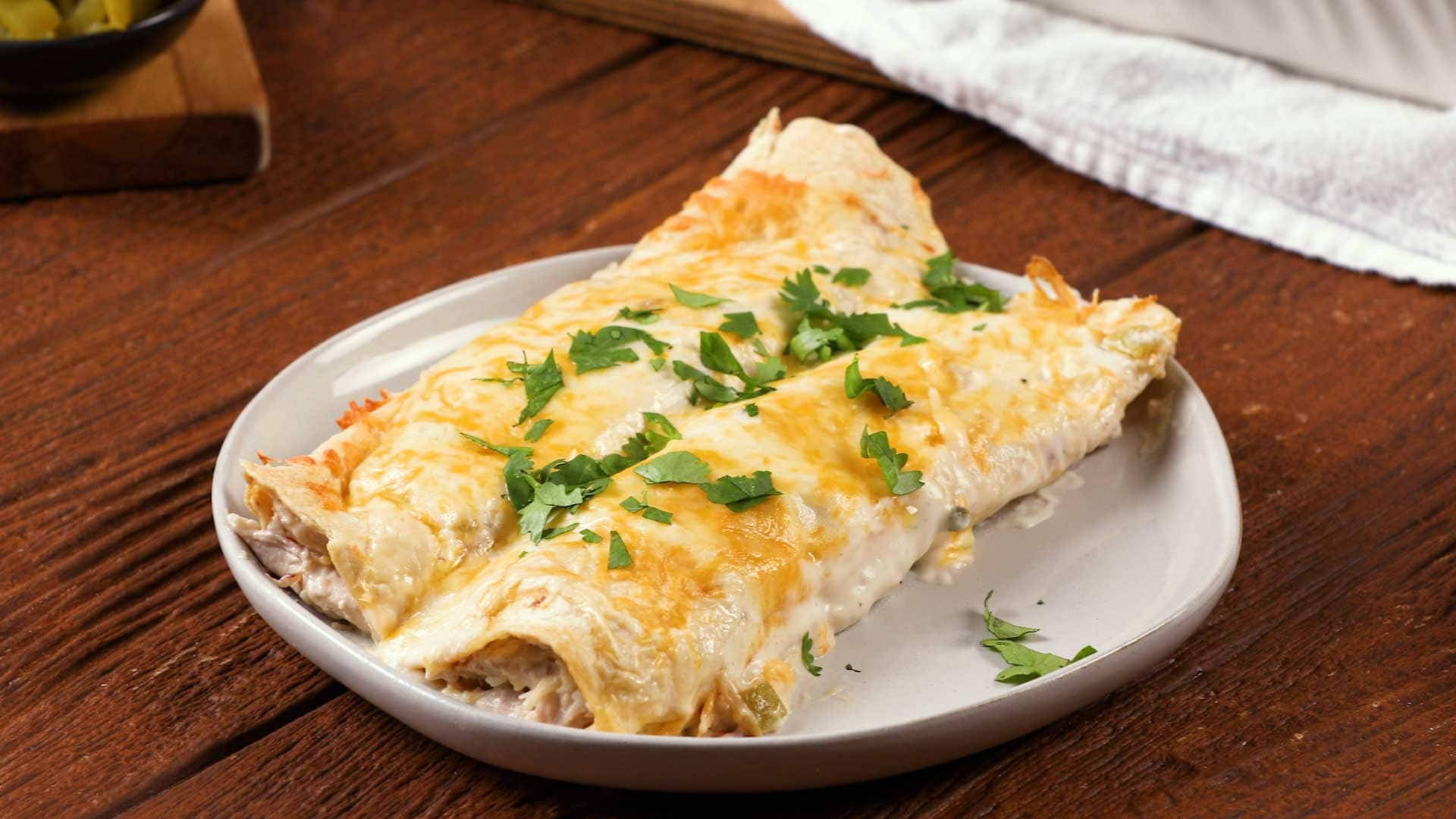 香脆乾燥 enchiladas 配新鮮香菜 壁紙 — 兩塊金黃色的雞肉玉米捲餅，上面覆蓋著融化的芝士和新鮮的芫荽，放在白色碟子上，置於鄉村風格的木桌上。