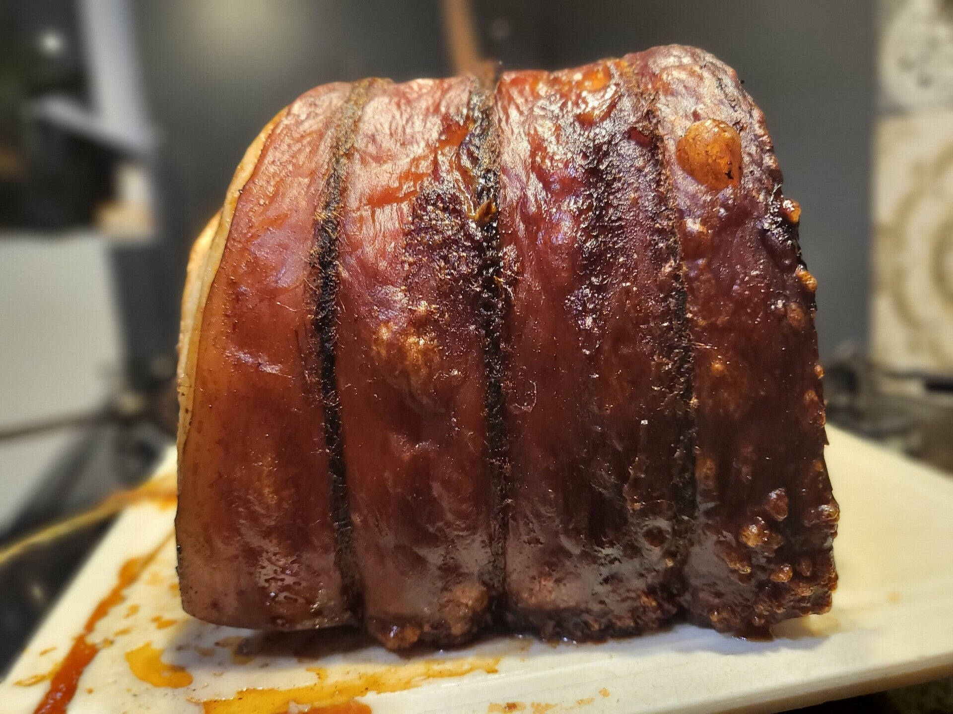 香脆豬腩烤肉盛宴 壁紙 — 特寫鏡頭：一塊木砧板上的烤豬肩肉，帶有焦糖化外皮和多汁質感，表面有光澤的釉面。