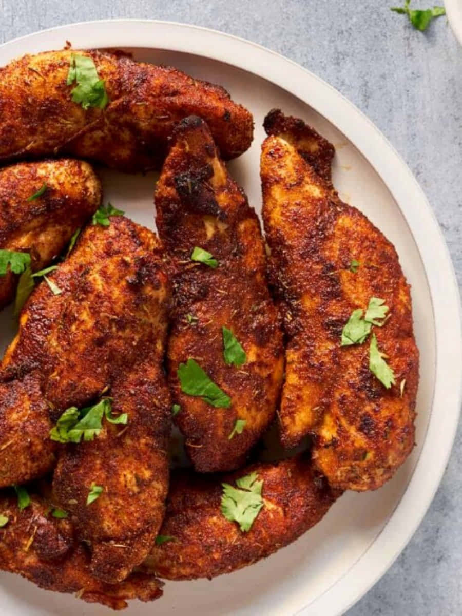 Blackened Chicken 桌布 壁紙 — 香脆辣味雞柳配上新鮮芫荽，堆疊在白色碟子上，置於灰色表面上。
