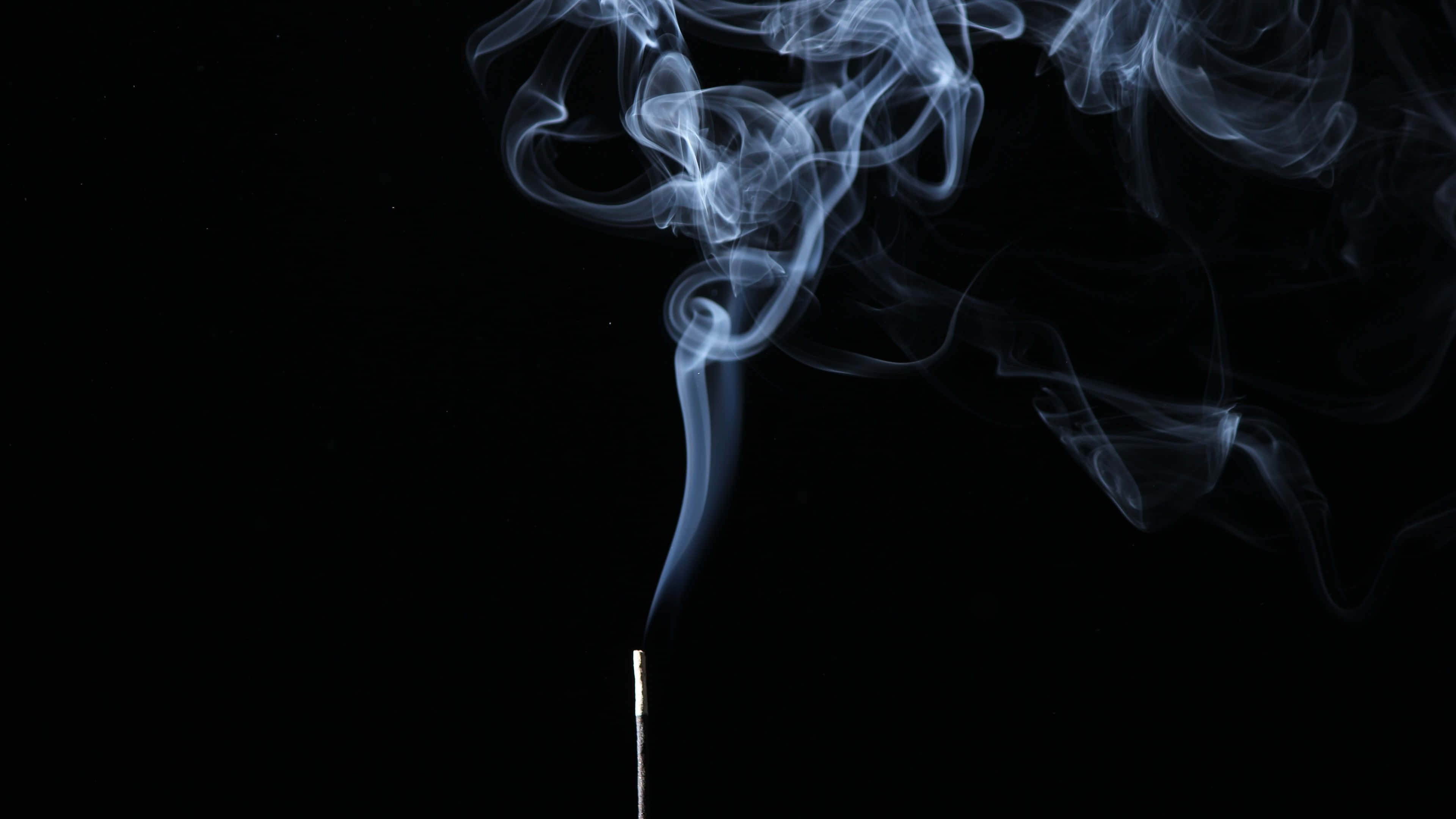 香薰白煙背景 壁紙 — 一支線香在純黑背景下散發出淡藍色的煙霧，形成旋轉的煙縷。