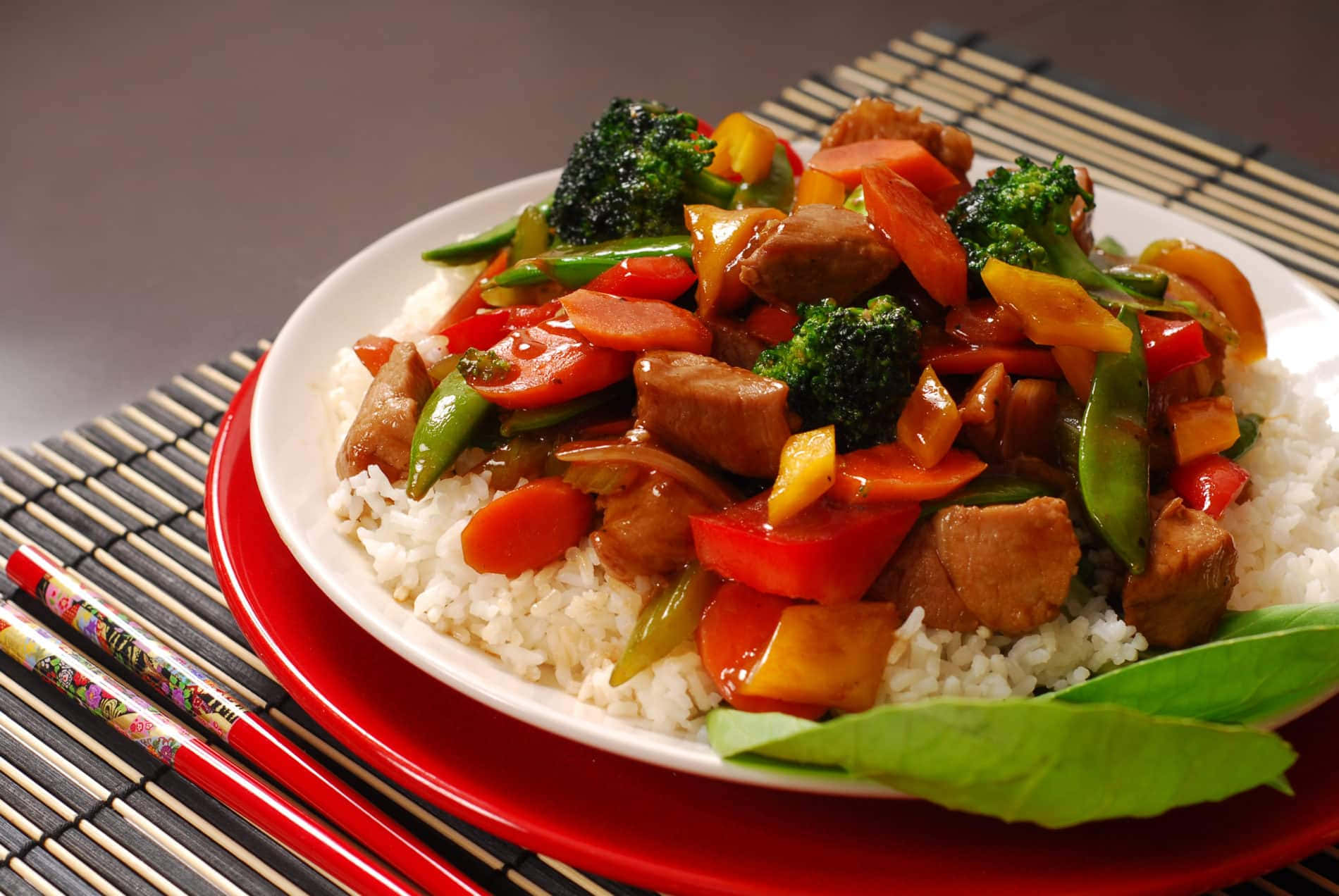 肉類蔬菜炒菜放在白飯上，用紅色碟子盛載，附上筷子。