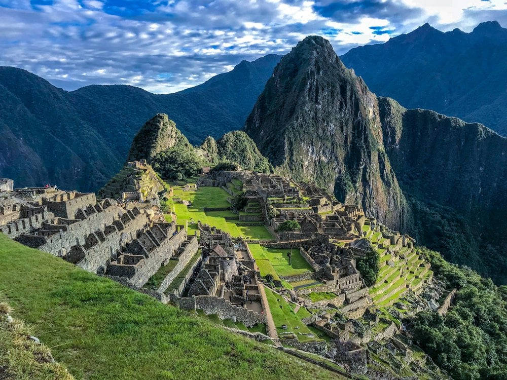 古老的印加遺址坐落在陡峭的綠色山脈之間，天空湛藍明亮。