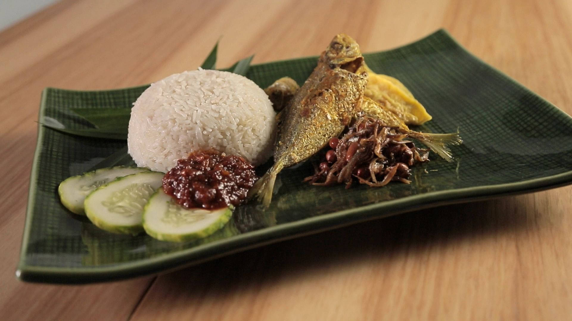 傳統亞洲菜餚，有米飯、魚、青瓜和醬汁，放在綠色盤子上。