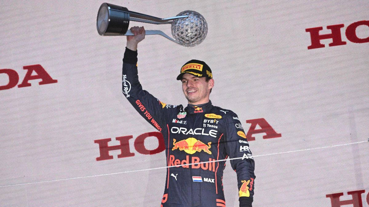 馬克·維斯塔潘 日本大獎賽舉杯 壁紙 — 一位微笑的賽車手穿著Red Bull賽車服，在頒獎台上勝利地將閃亮的獎盃高舉過頭頂。