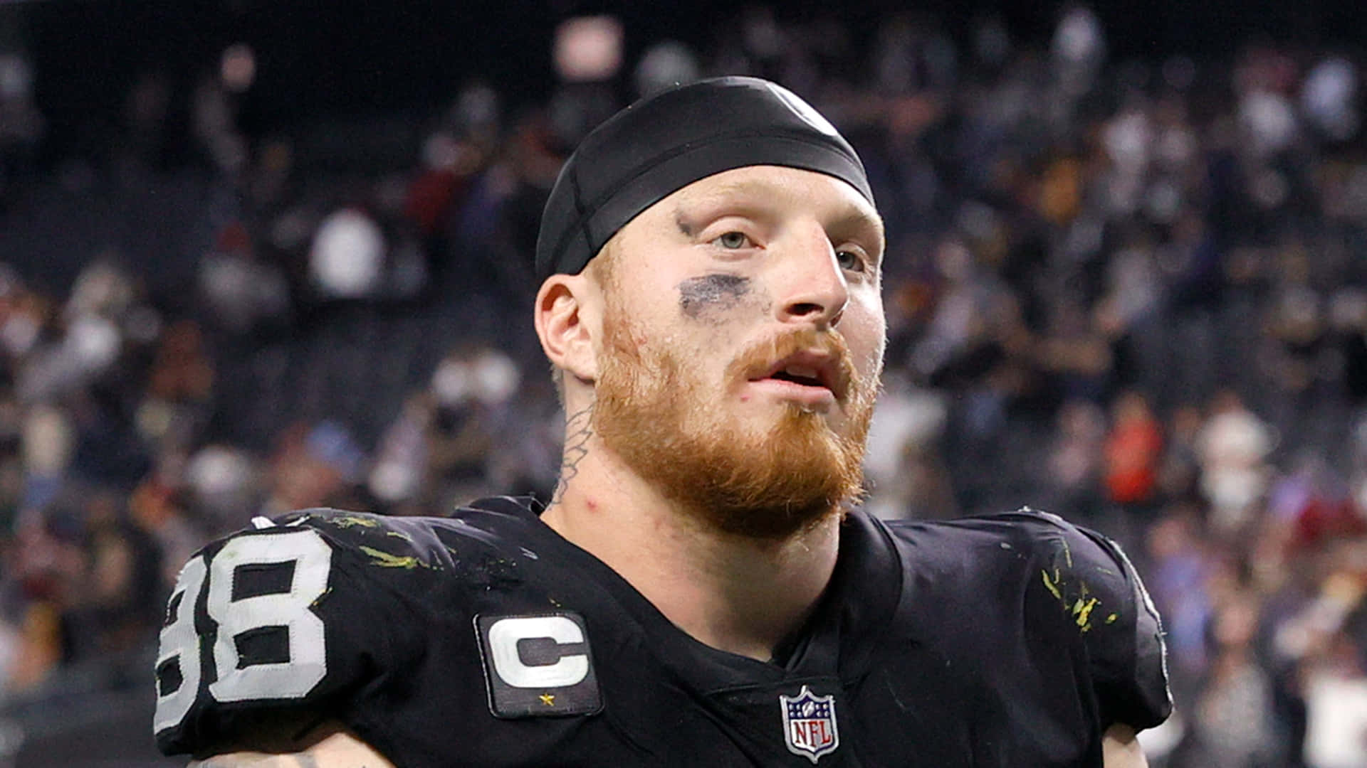 NFL足球運動員留鬍子，黑色球衣上有隊長臂章，夜間比賽。