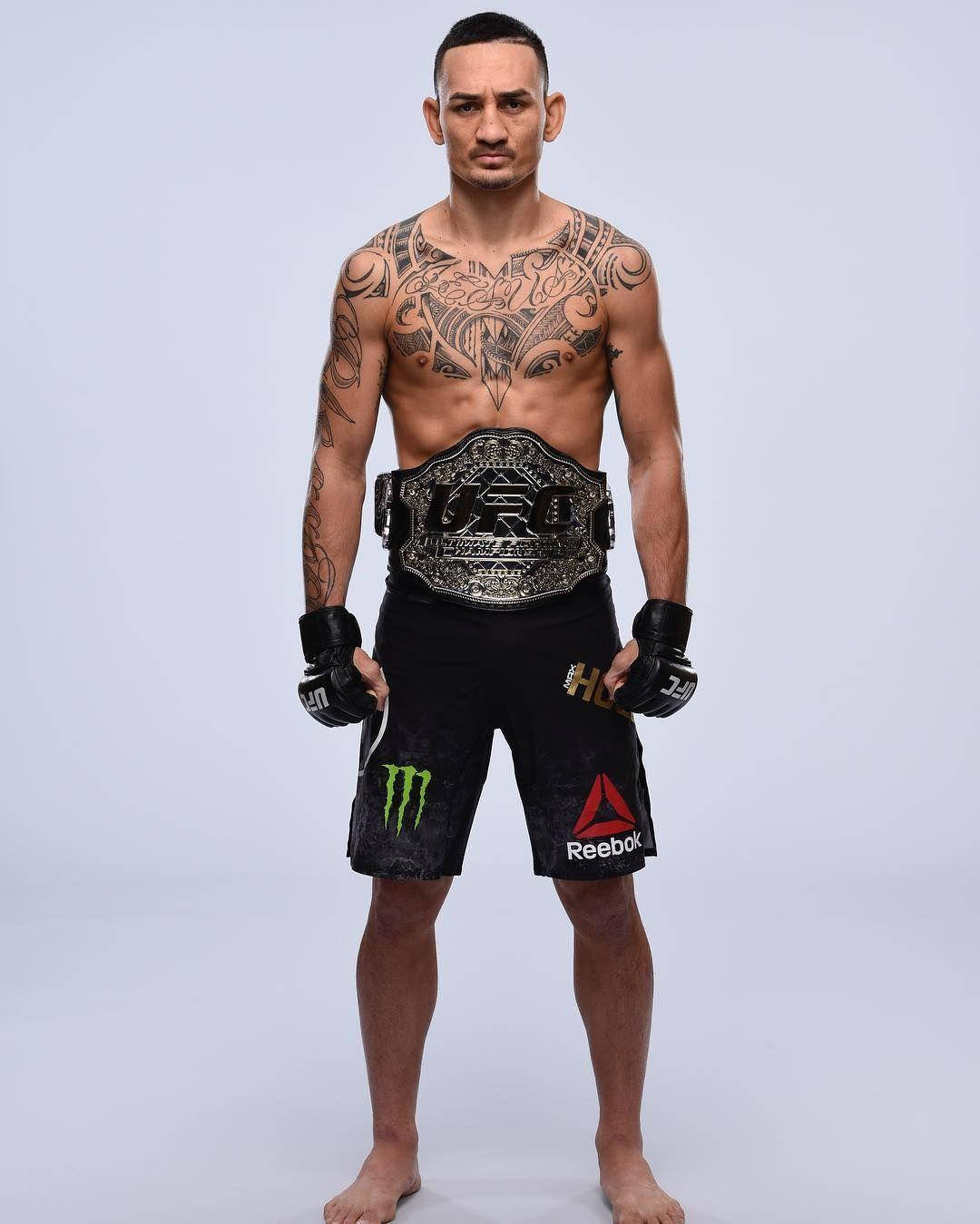 一位有紋身的男性MMA拳手在攝影棚中手持冠軍腰帶。
