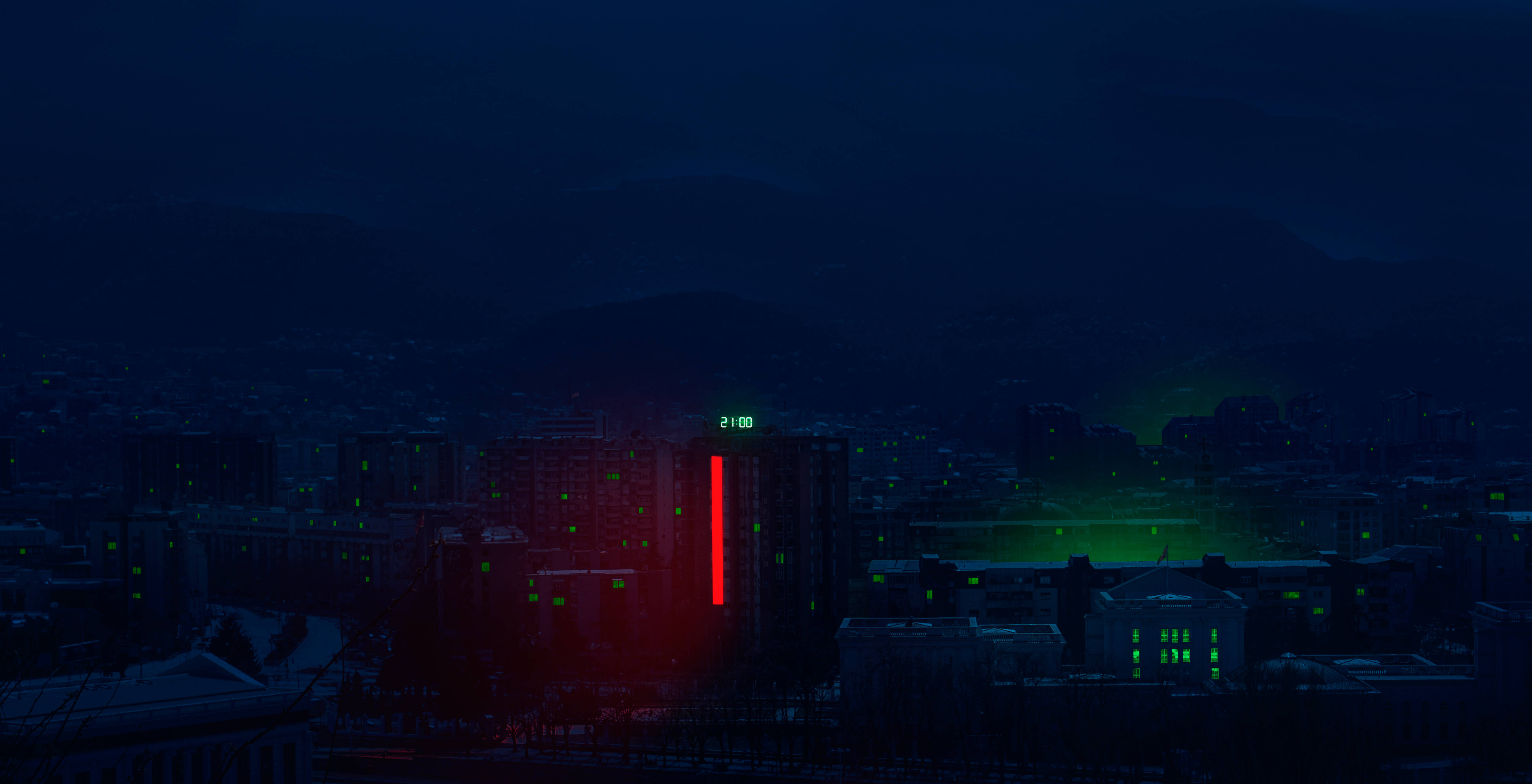 馬其頓時鐘大樓 壁紙 — 夜晚的黑暗城市景觀，一座高樓發出紅色和綠色的光芒，背景是遠山。