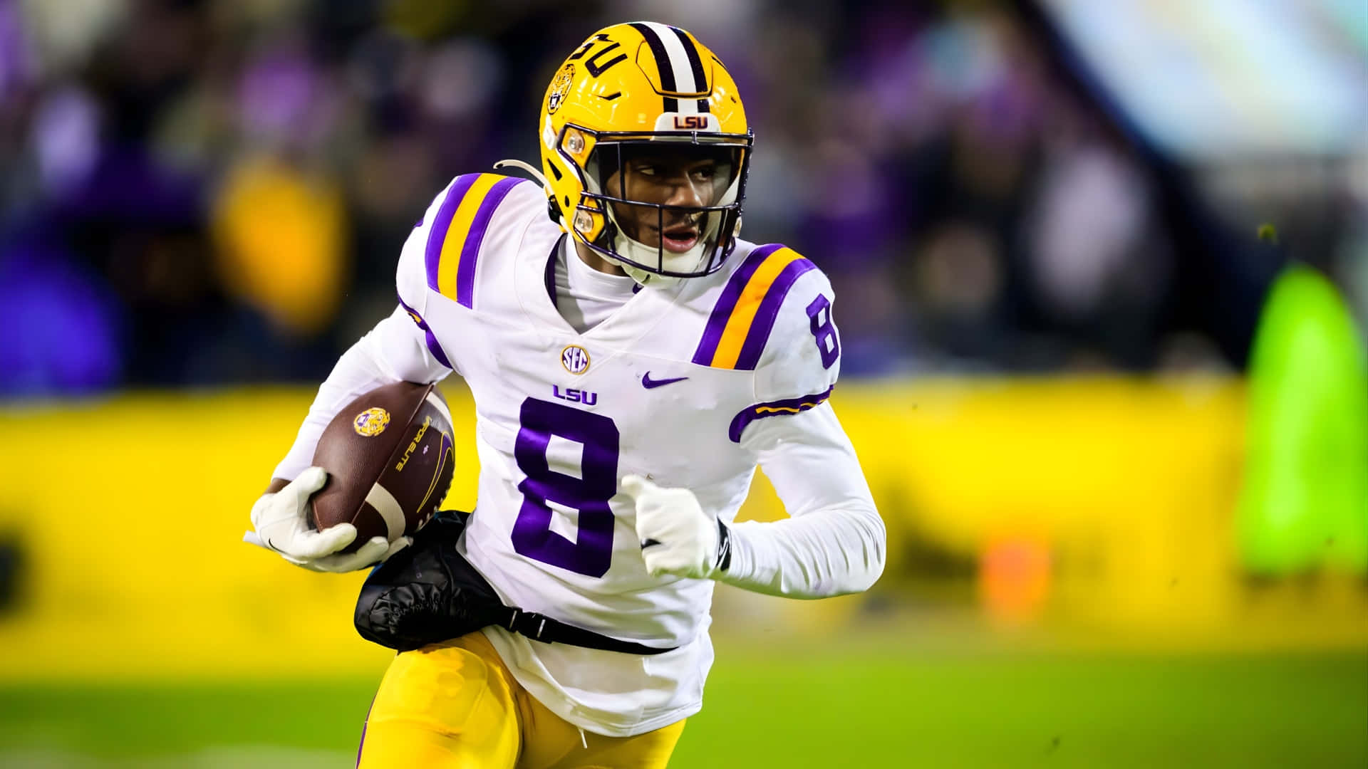 馬利克·納伯斯 LSU 精彩高光 壁紙 — 一名身穿白色和紫色裝備的LSU足球員在夜間比賽中，在體育場燈光下帶球衝刺。