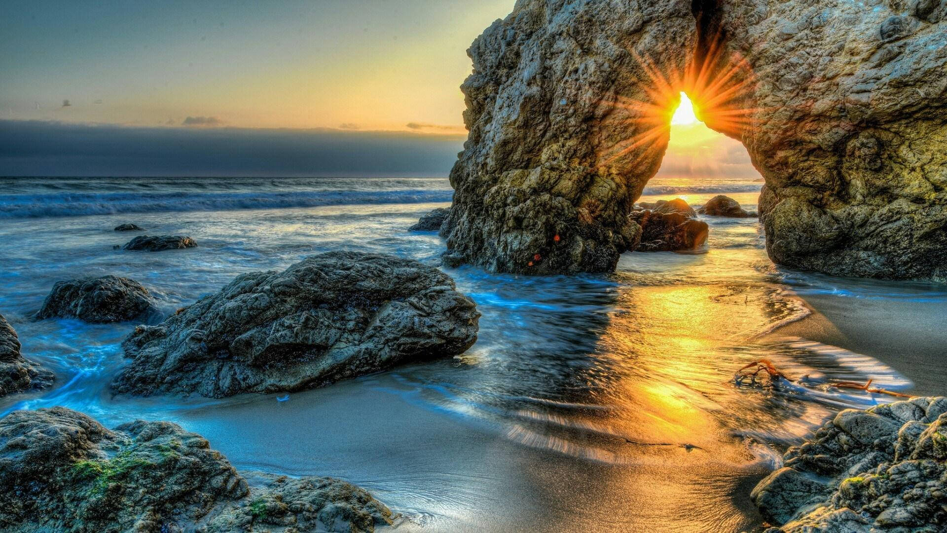 夕陽光芒穿過岩石海灘上的岩石拱門，伴隨海浪。