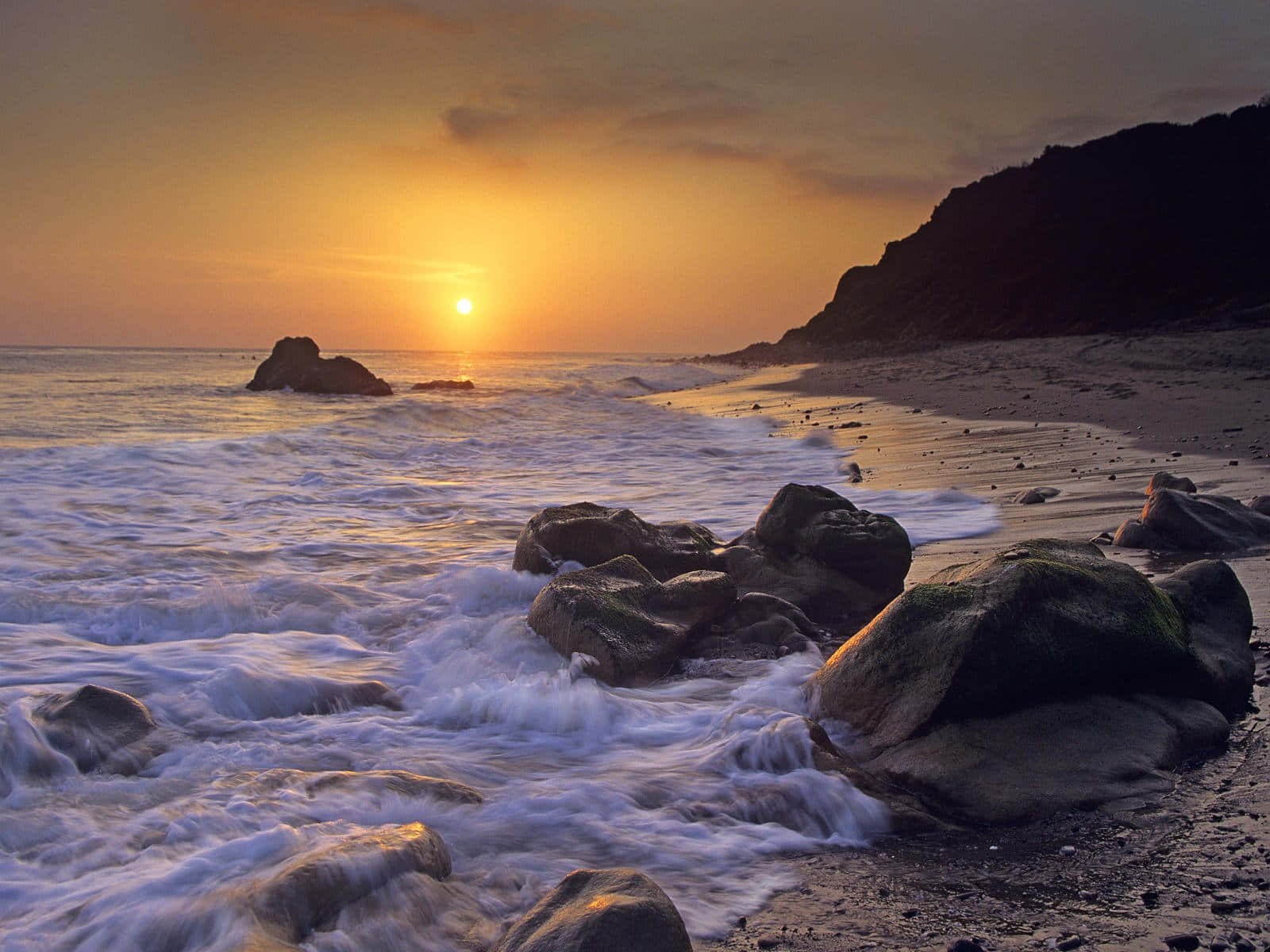 海上夕陽，海浪拍打懸崖旁的岩石海灘