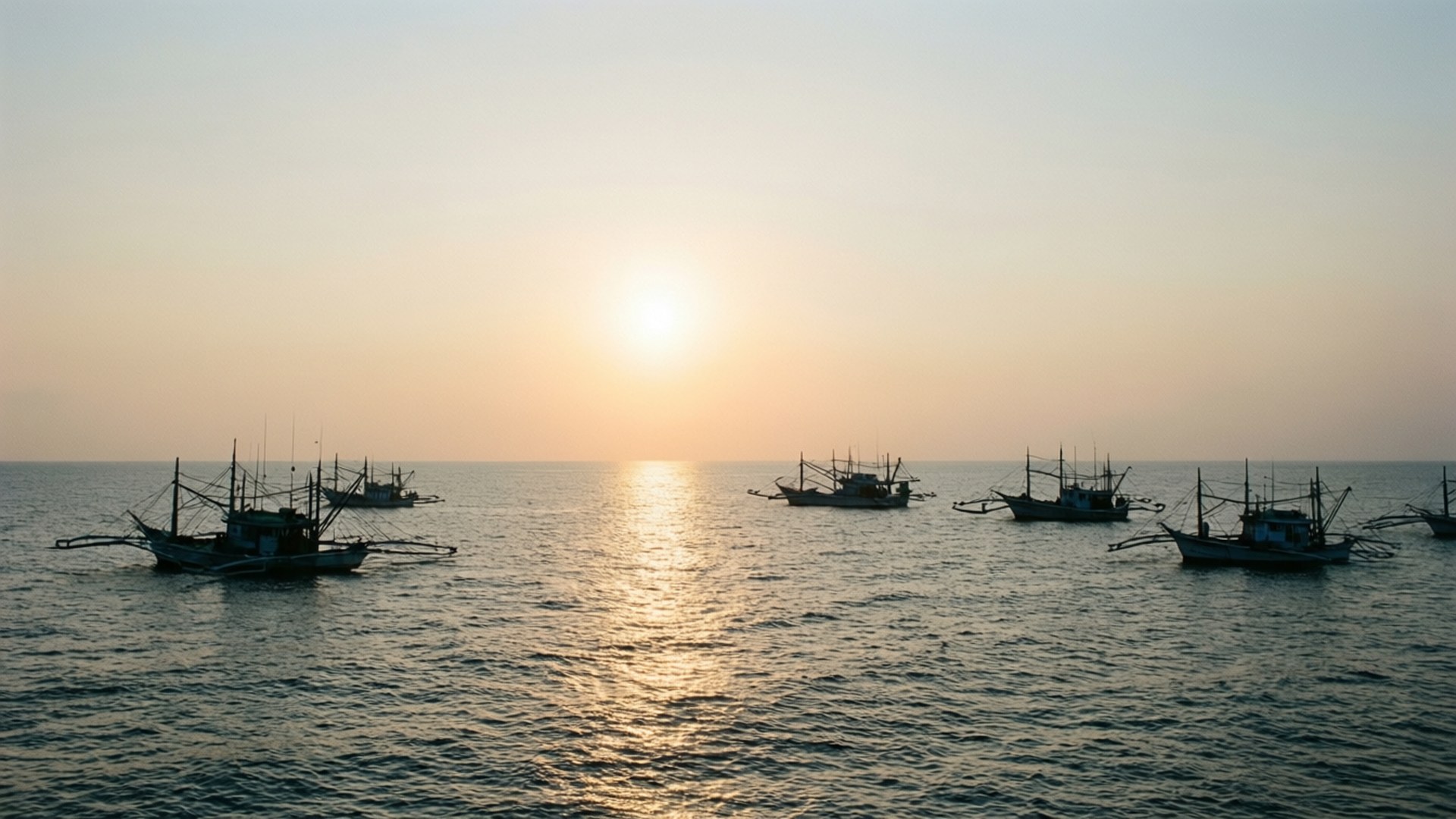 馬尼拉海岸日出 壁紙 — 剪影的漁船在海洋上平靜漂浮，夕陽散發溫暖的金色光芒。