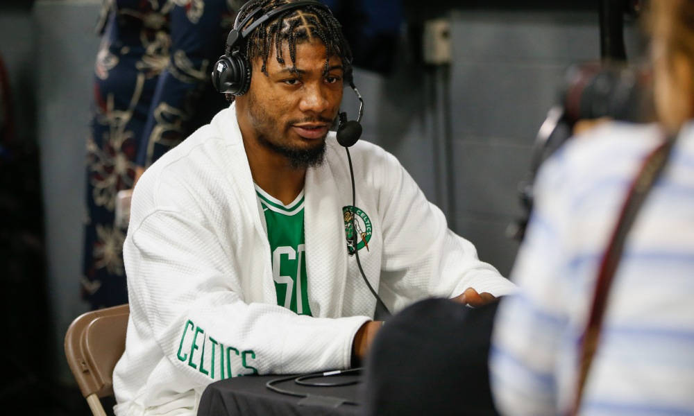 馬庫斯·史馬特賽後接受訪問 壁紙 — 一名身穿白色Celtics連帽衫和耳機的籃球運動員在昏暗的房間裡專注地坐著接受媒體採訪。