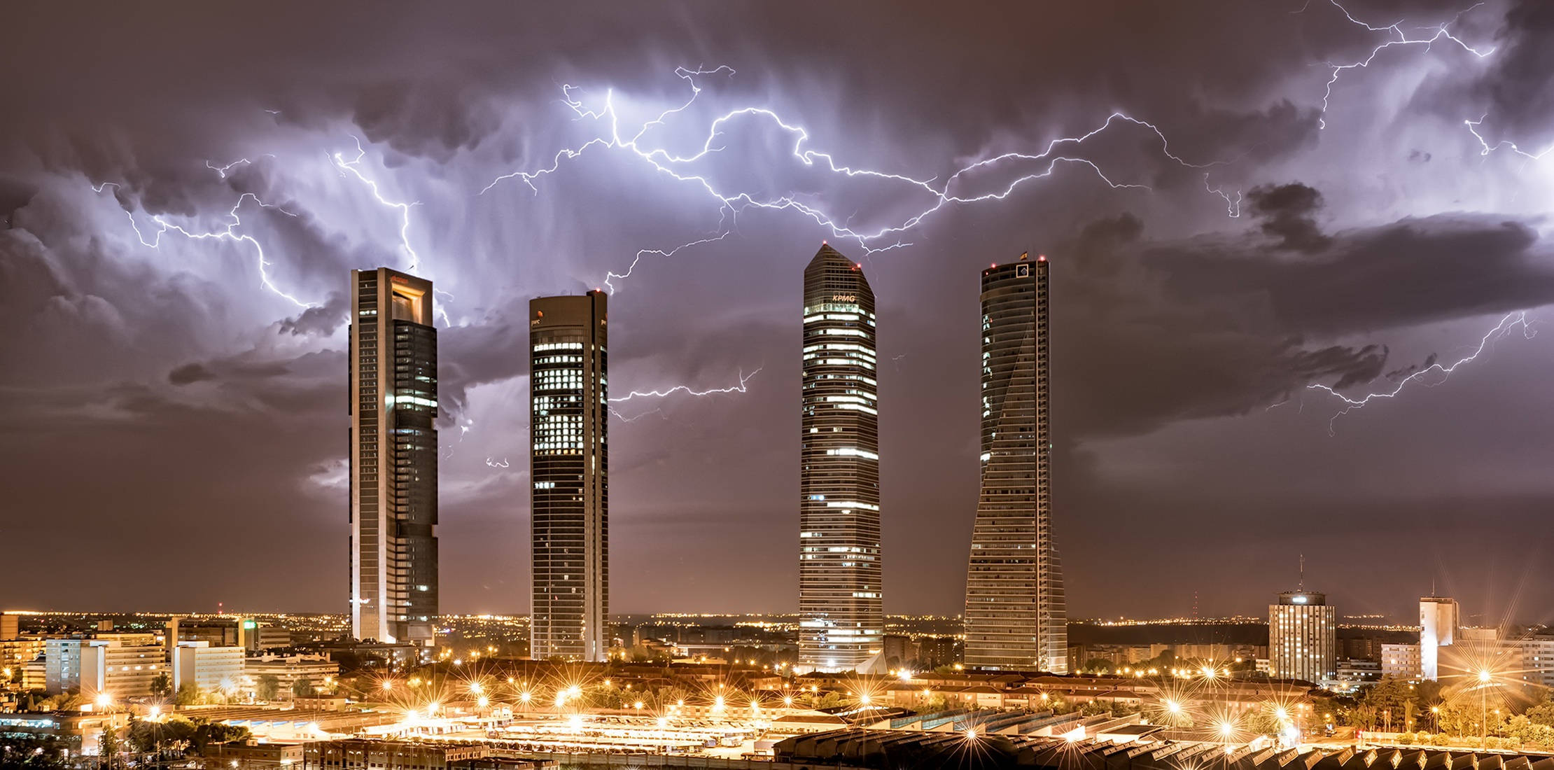 馬德里四塔夜景 壁紙 — 四座高聳的摩天大樓在暴風雨的夜晚，在充滿生動閃電的戲劇性天空下被照亮。