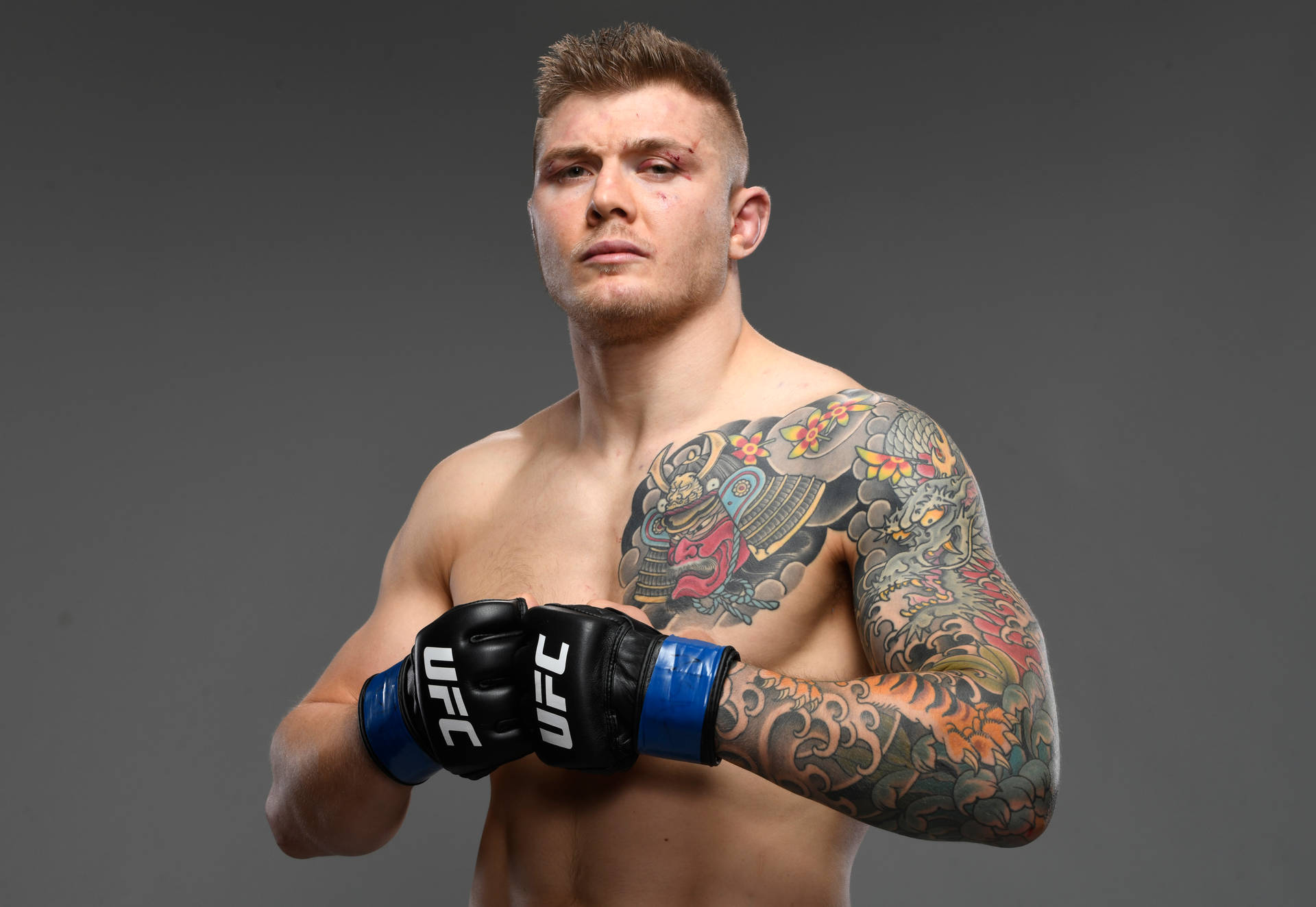 一名有紋身的男性UFC戰士戴著手套在攝影棚中嚴肅地擺姿勢。