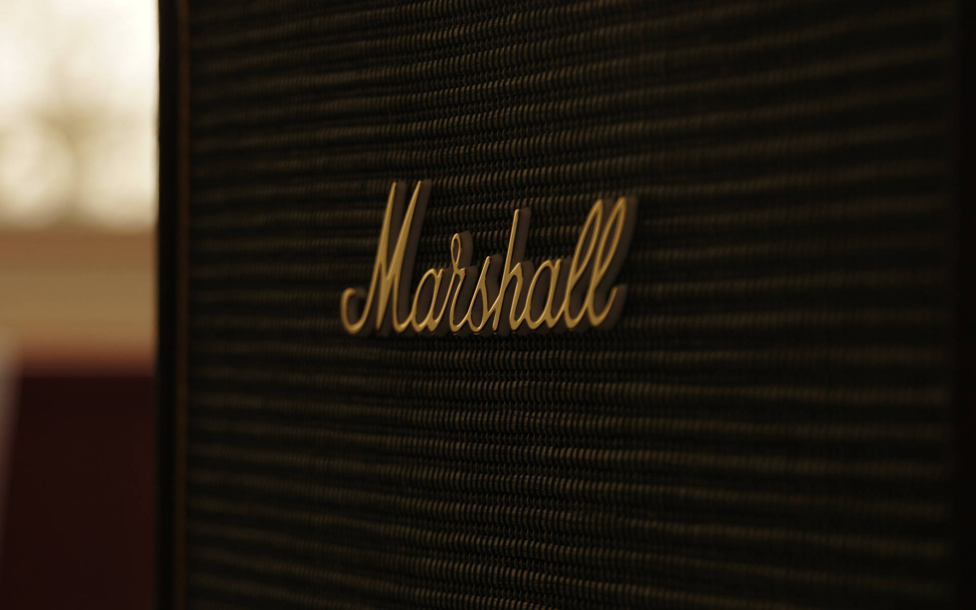 馬歇爾擴大機標誌印於音箱 壁紙 — Marshall擴音器特寫，金色標誌位於紋理黑色格柵上，背景溫暖模糊。