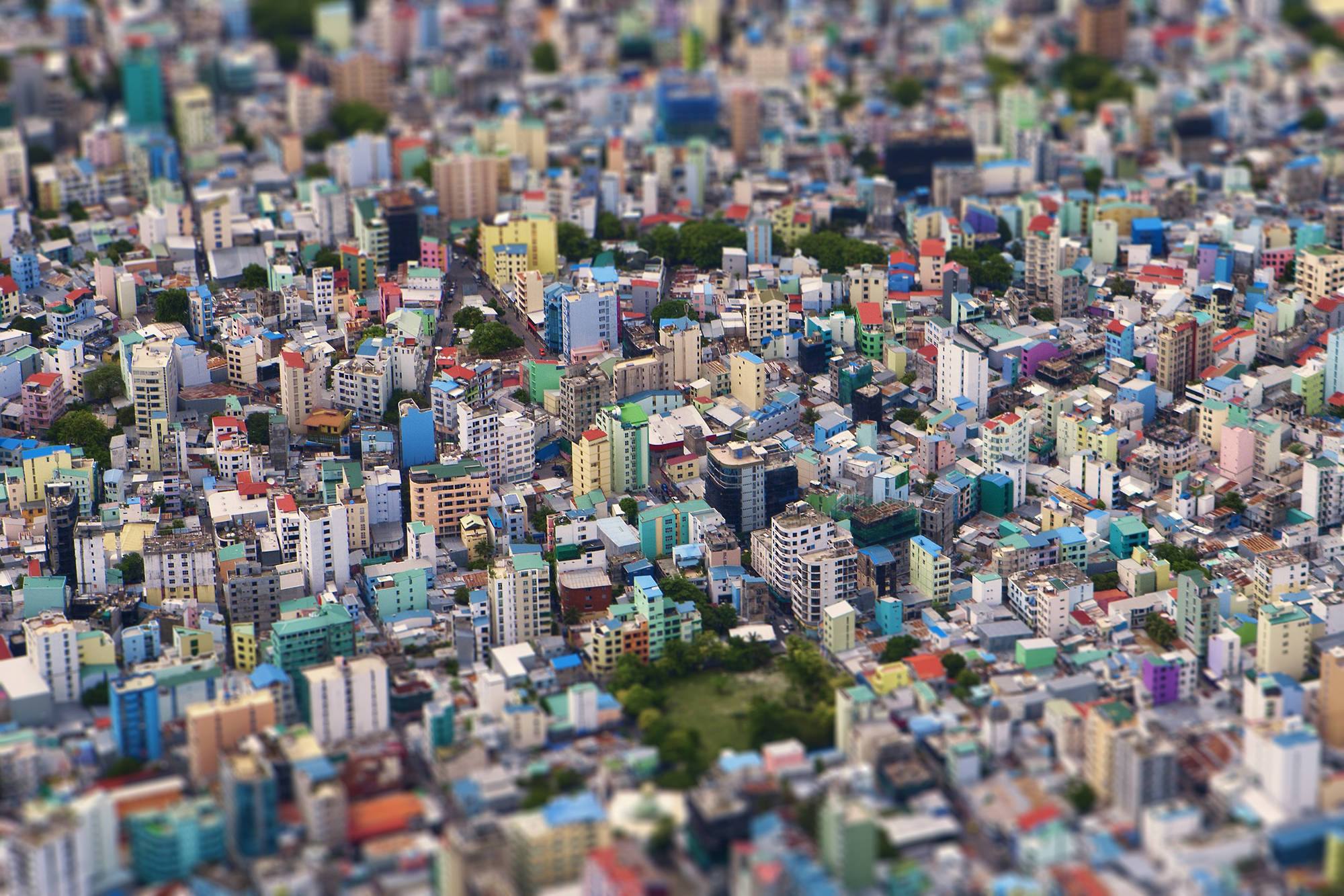 馬爾代夫城市風景背景 壁紙 — 在明亮的日光下，密集的城市景觀中色彩繽紛的建築物和綠色地塊的鳥瞰圖。