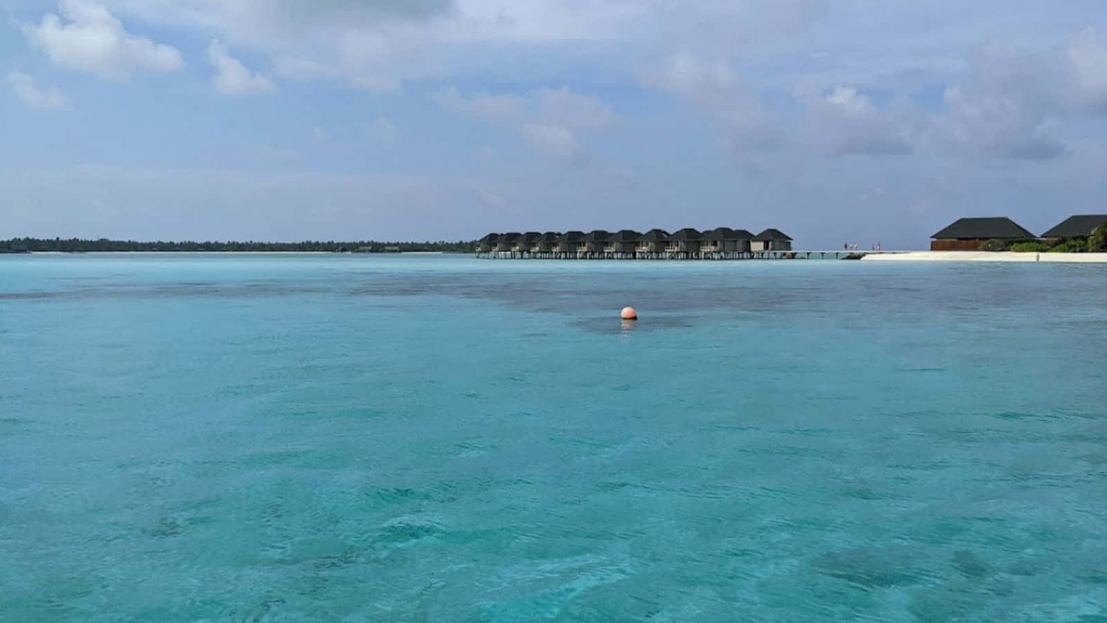 馬爾地夫的完美碧藍海水 壁紙 — 清澈碧綠的海水延伸到水上平房，上方是部分多雲的藍天。