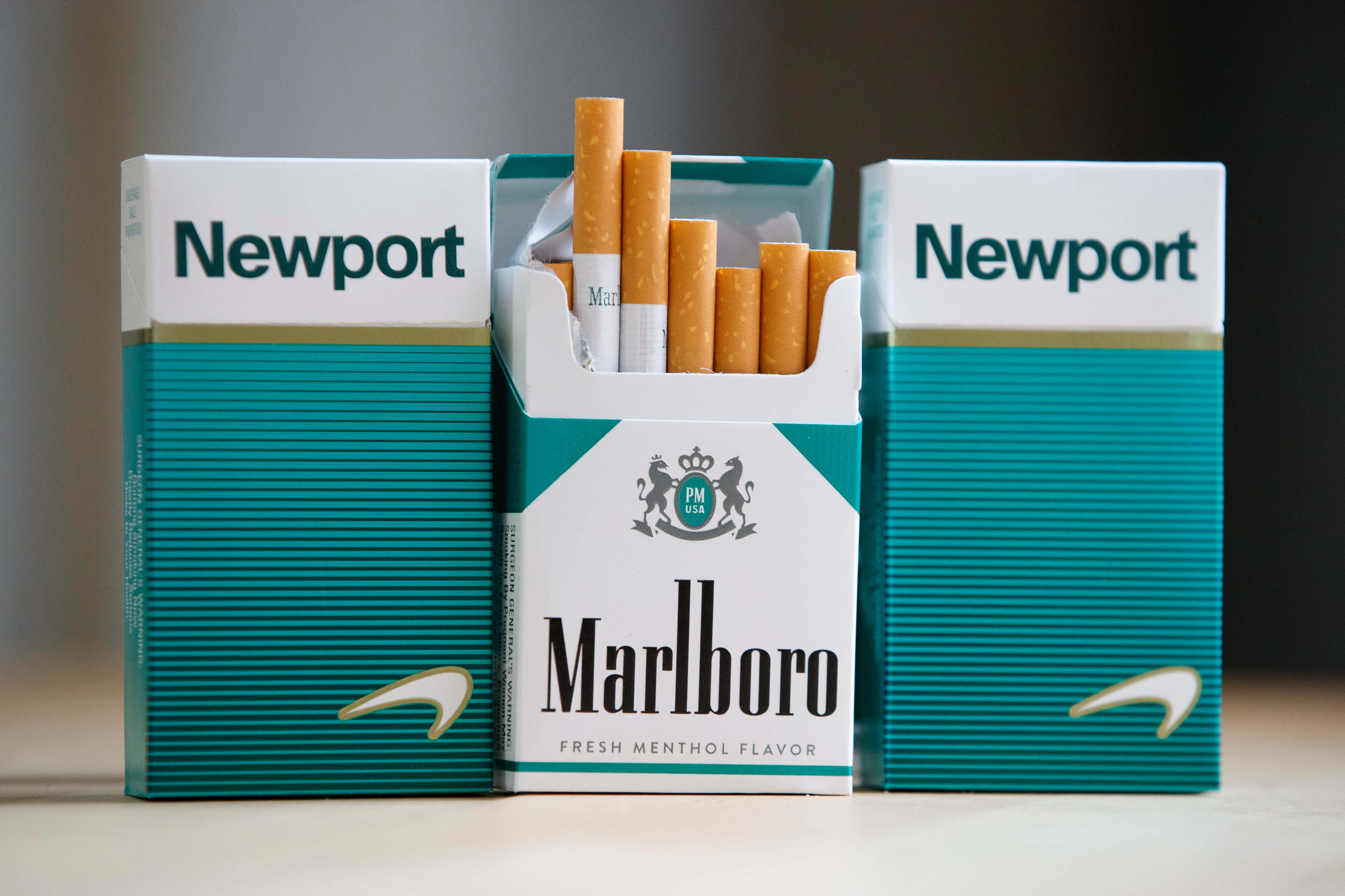 馬爾堡新ports香煙圖 壁紙 — 三個香煙包，包括一個萬寶路薄荷煙包，香煙散落在模糊的背景上。