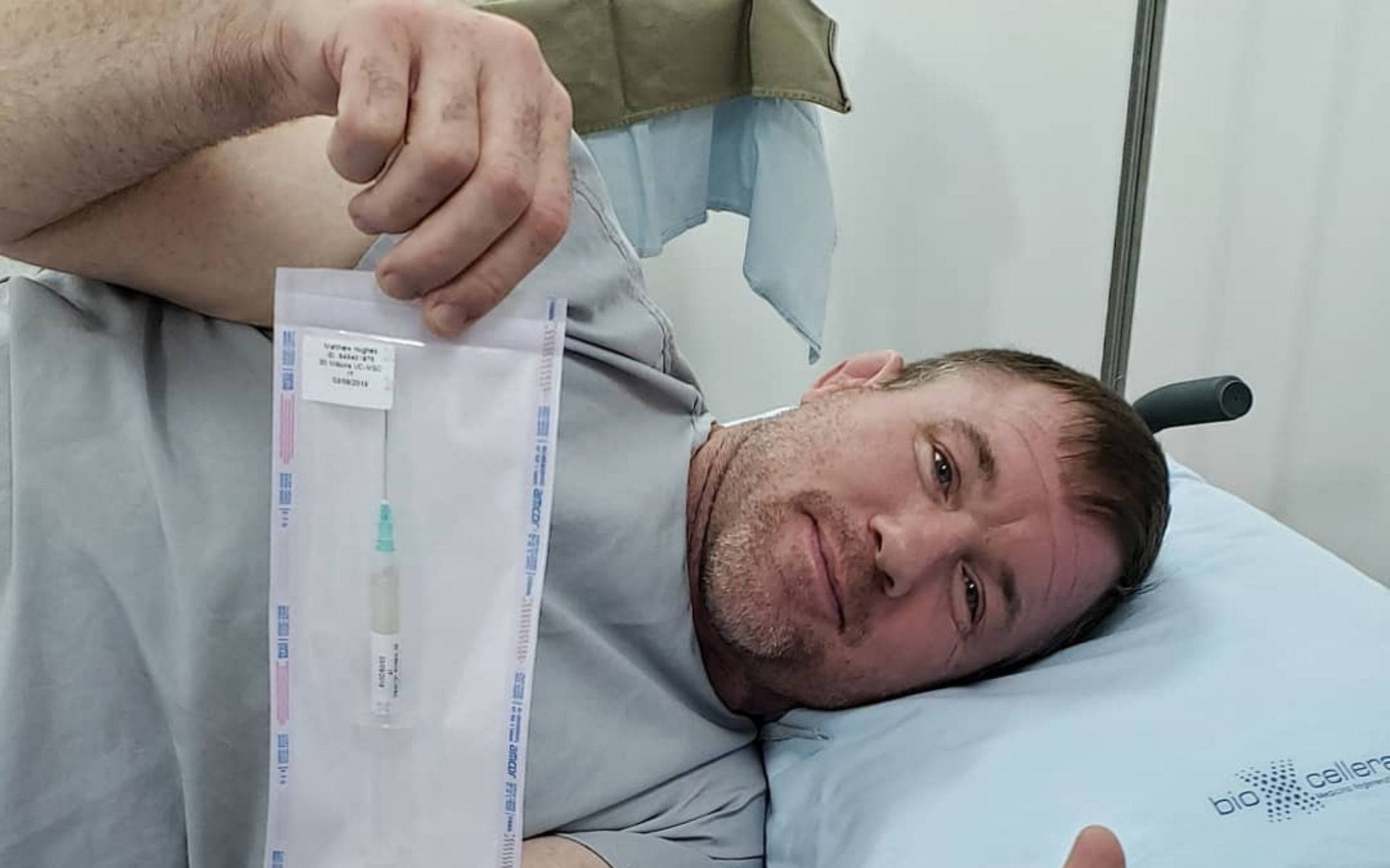 馬特·休斯在醫療床上 壁紙 — 一名男子在醫院病床上，手持密封醫療包裝內的注射器，望向鏡頭。