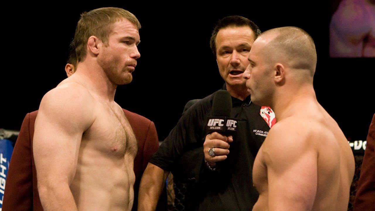 兩位赤裸上身的MMA拳手在UFC比賽前互相凝視，裁判手持麥克風。