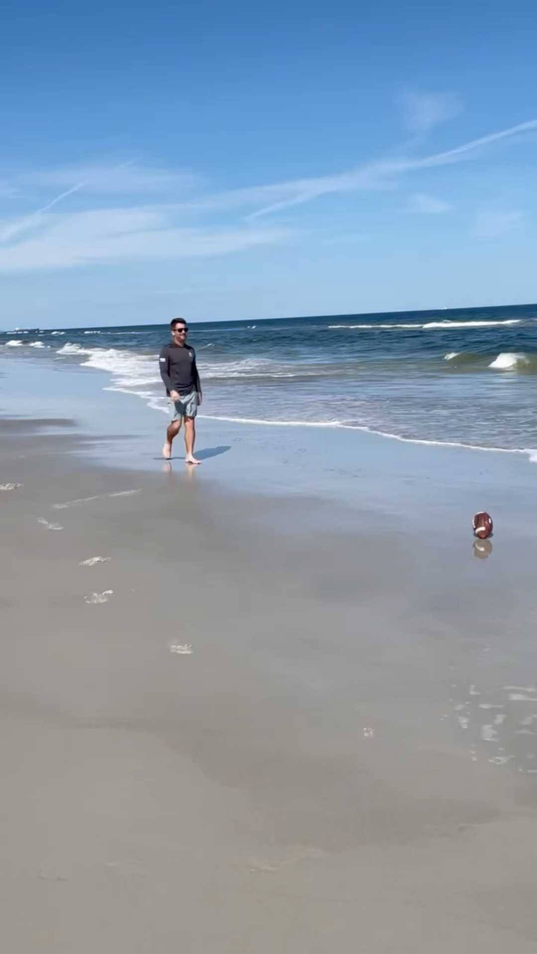 男子在海灘上赤腳行走，伴隨著海浪和晴朗的藍天。