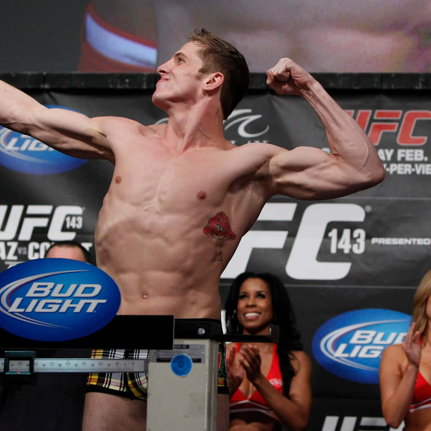 馬特·里德爾於UFC 143賽事稱重儀式 壁紙 — 一位肌肉發達的UFC拳手在稱重活動中勝利地展示肌肉，身後有粉絲歡呼。