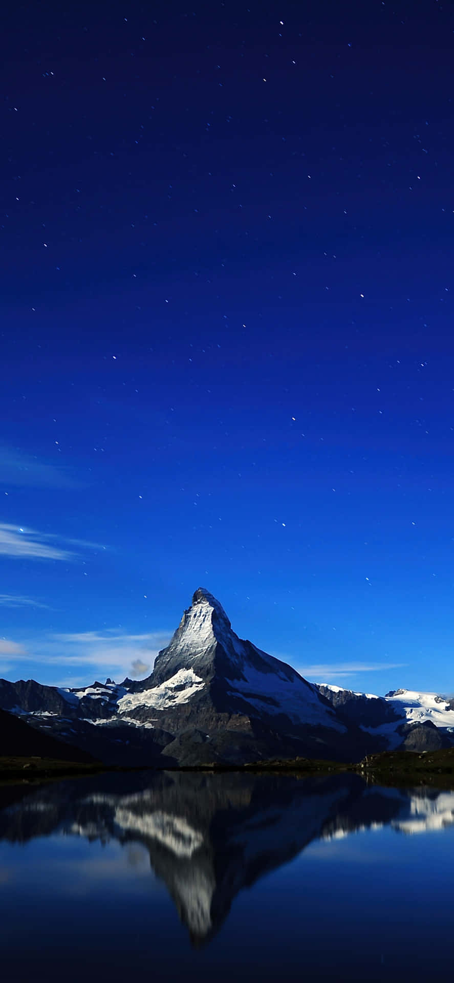 在繁星點點的夜空下，平靜的水面倒映著雪山山峰。