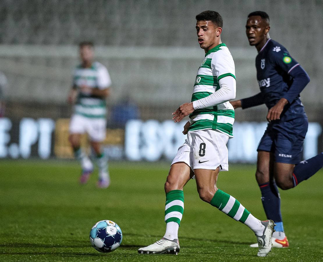馬特烏斯·努內斯身穿 Sporting CP 球衣的全身照 壁紙 — 一名身穿綠色和白色條紋的足球運動員在球場燈光下的草地上運球，球是藍白相間的。