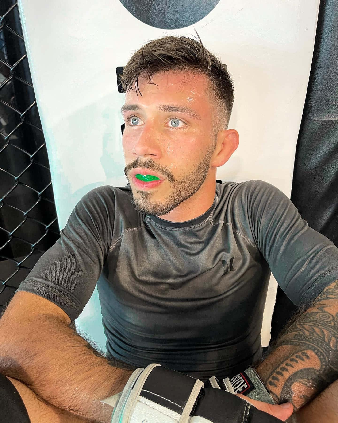 嘴上塗著綠色顏料的運動員在訓練後於MMA籠中休息。