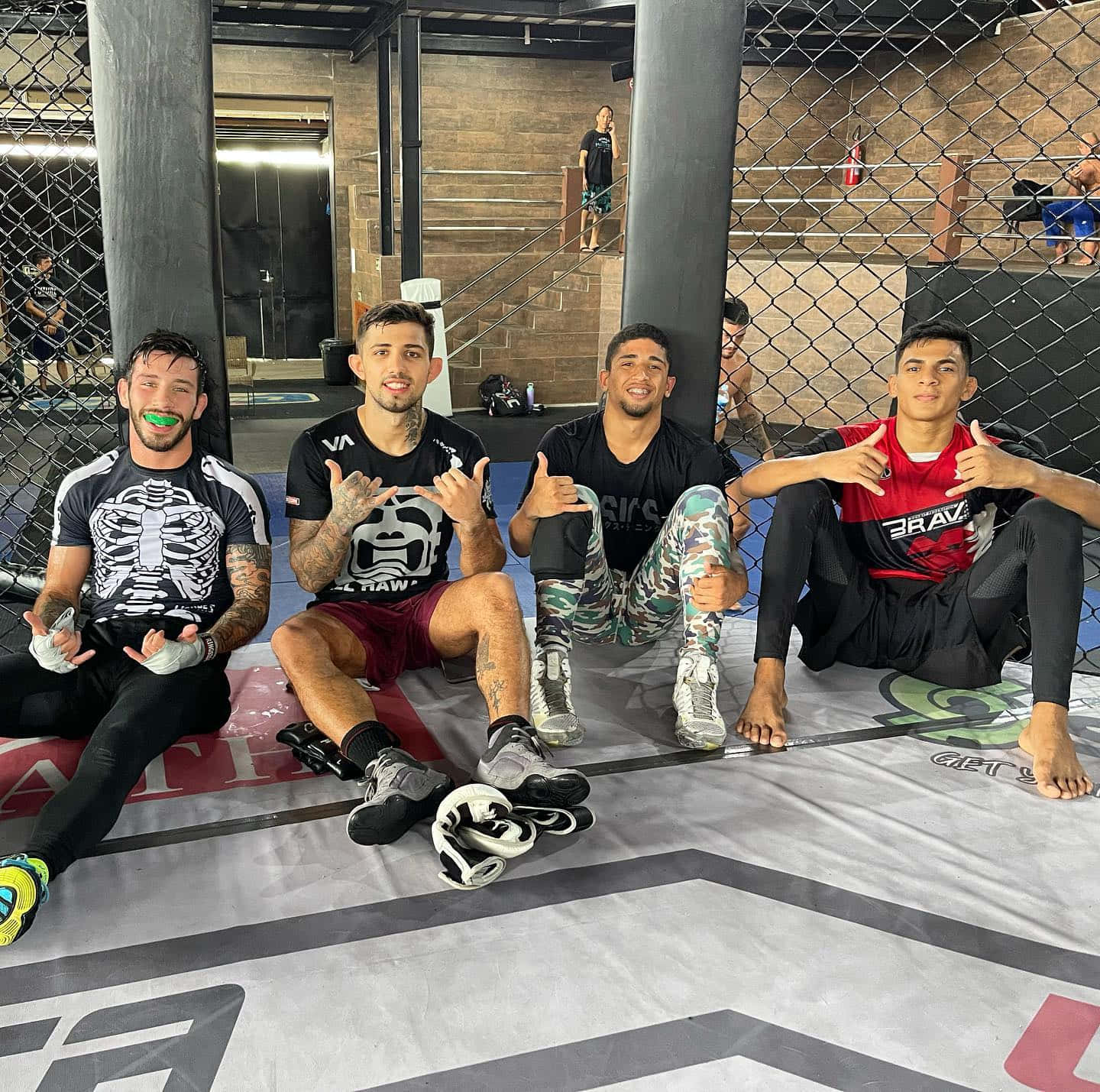 四名男性MMA拳手在健身房的籠墊上擺姿勢。