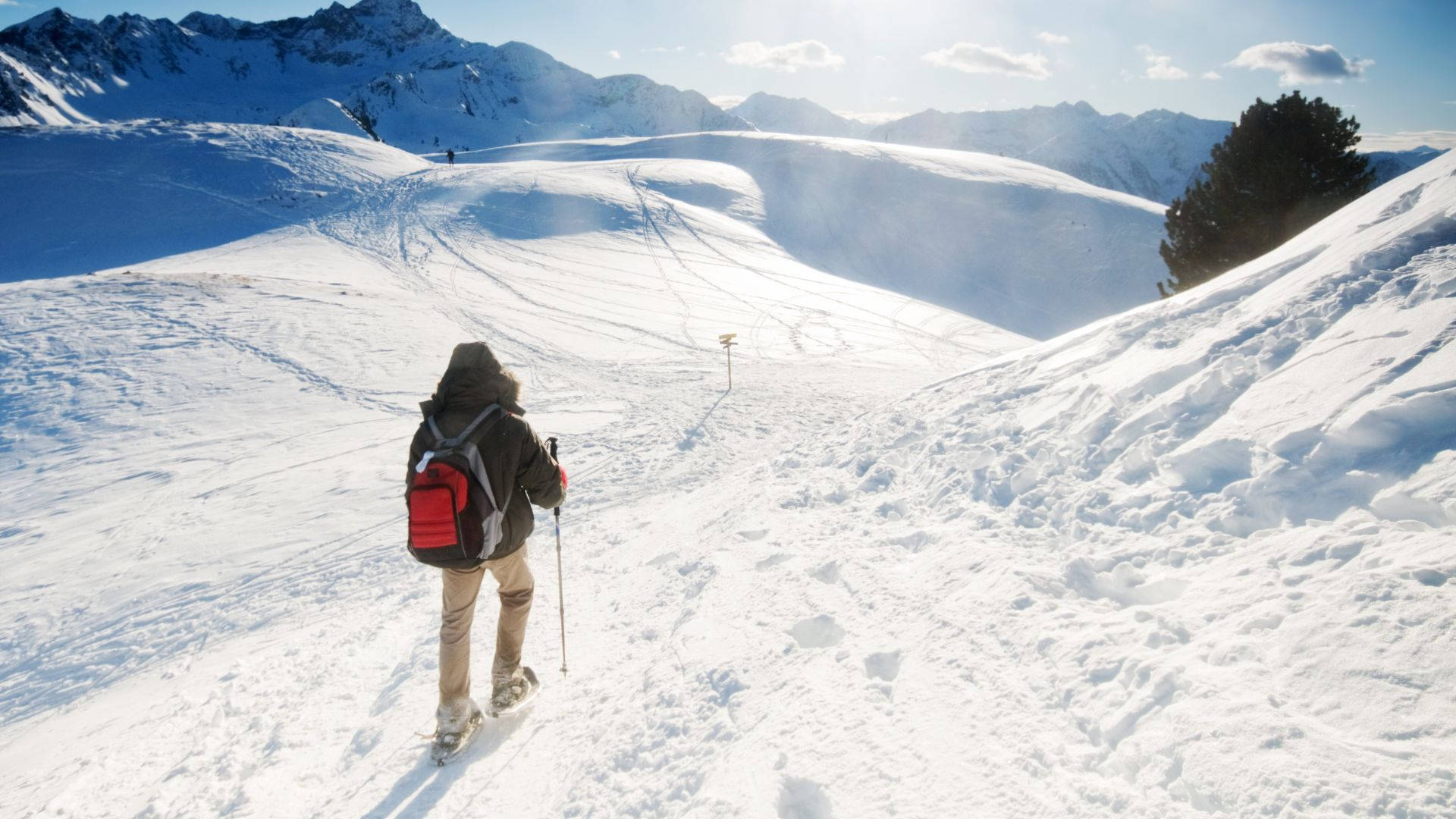 滑雪者在明媚陽光下背著紅色背包攀登雪山斜坡。